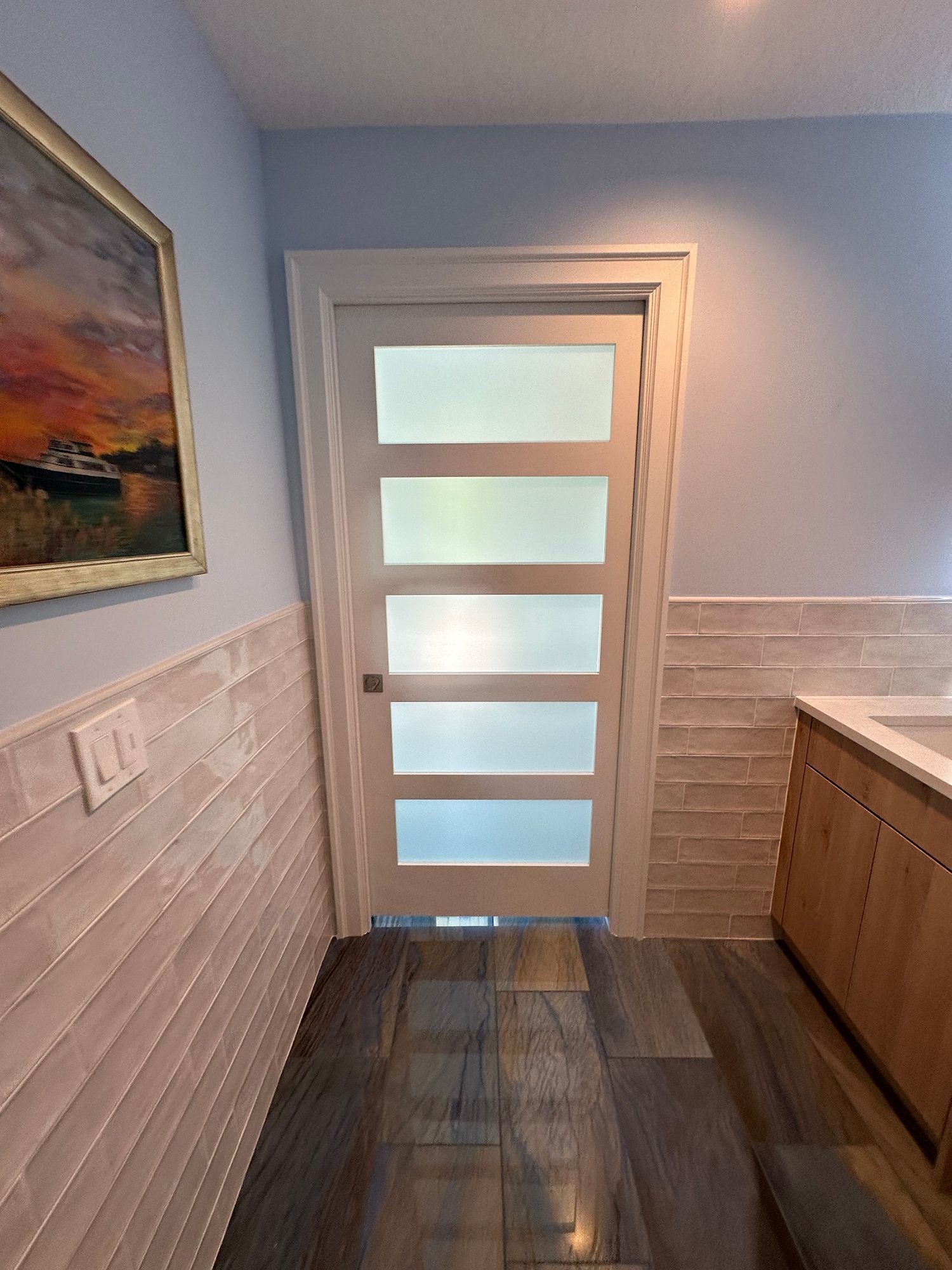 Bathroom door with frosted glass panels, surrounded by white trim, light blue walls, and tiled accents.