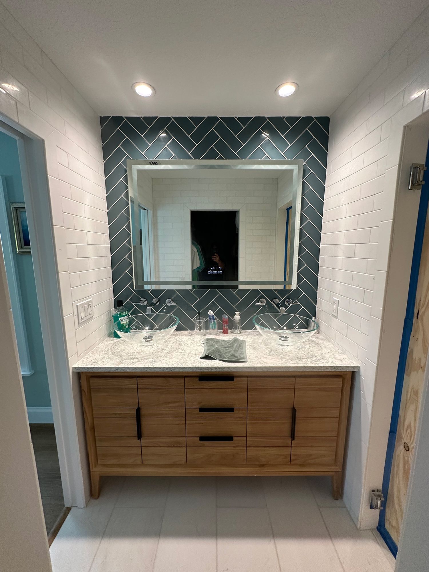 Bathroom with wooden vanity, herringbone tile accent wall, large mirror.