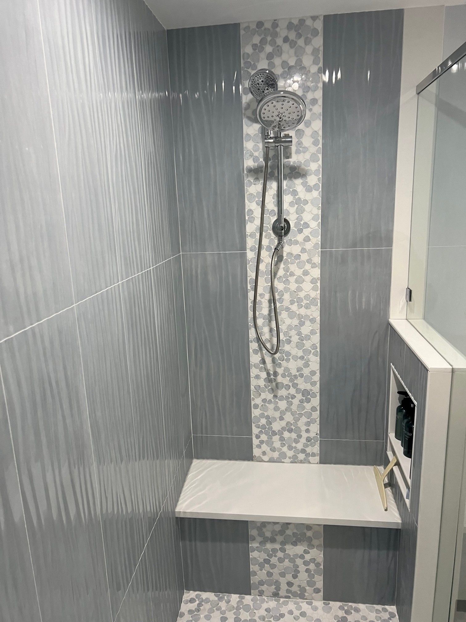 Gray tiled shower with a white bench, mosaic accent, and silver shower head.