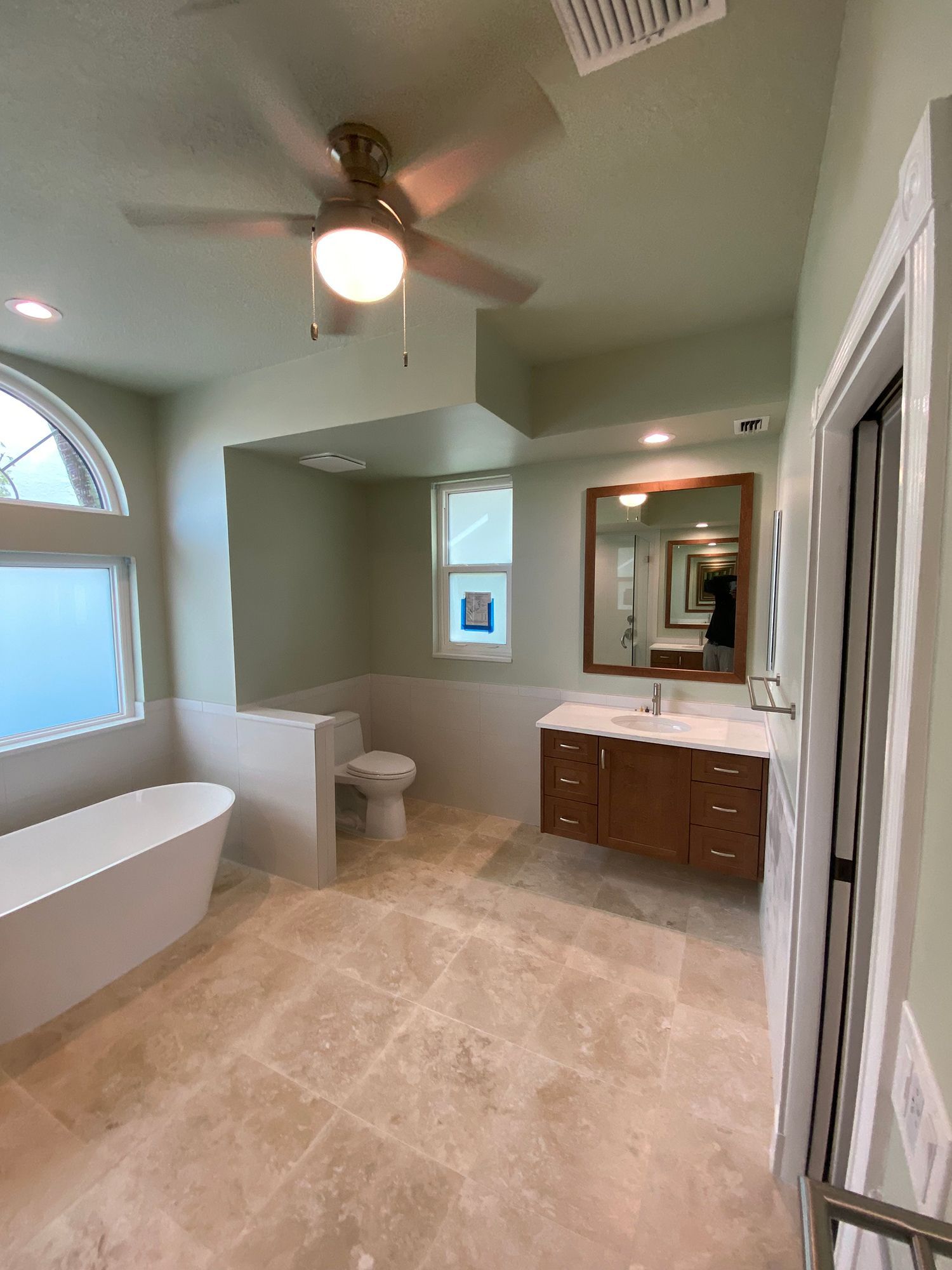Spacious, light green bathroom with a freestanding tub, toilet, vanity, and large mirror.