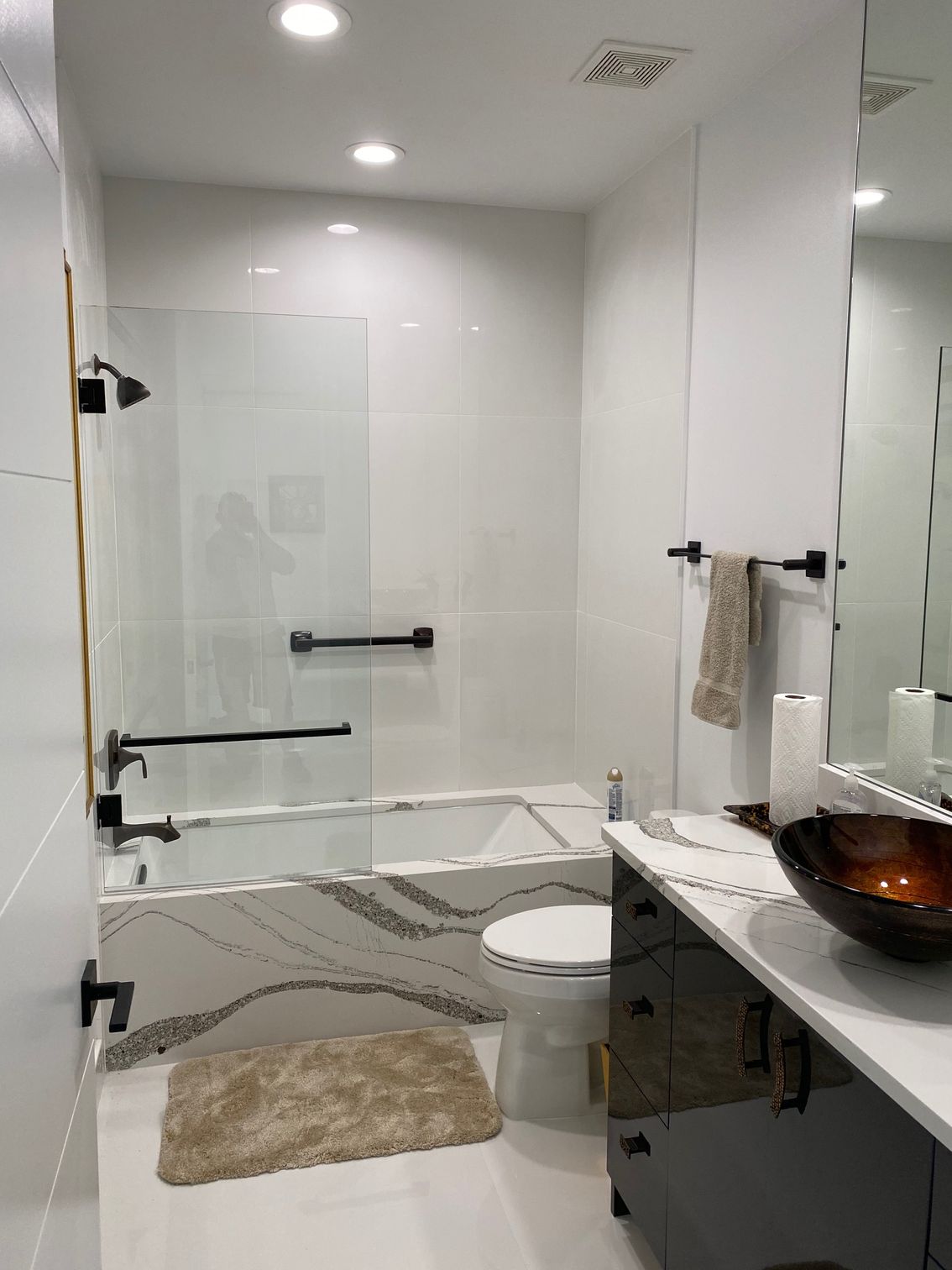 Modern white bathroom with a glass shower enclosure and black fixtures.