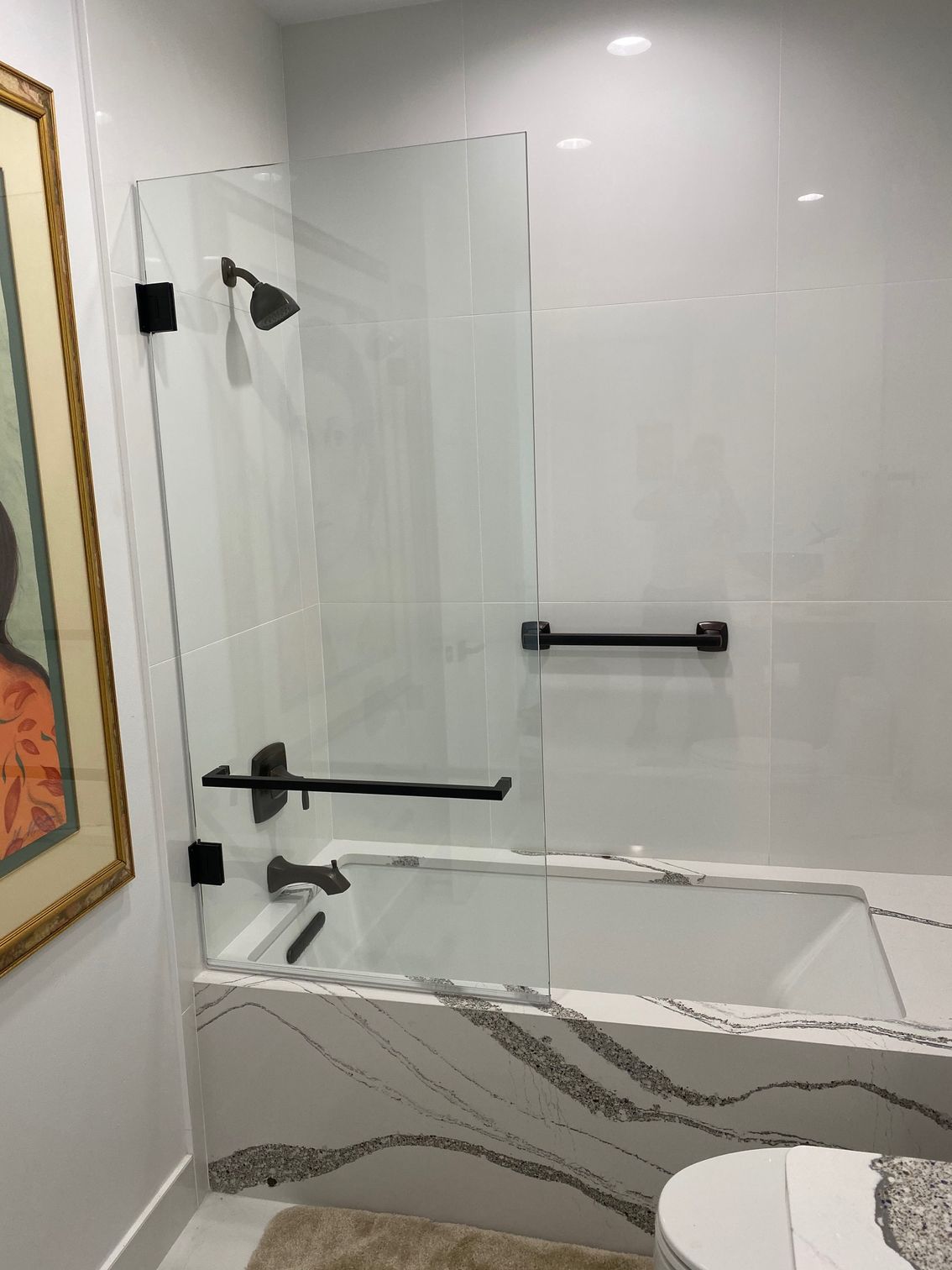 Bathroom with white tile walls and a tub with a glass shower screen, black fixtures, and a marble-patterned tub surround.