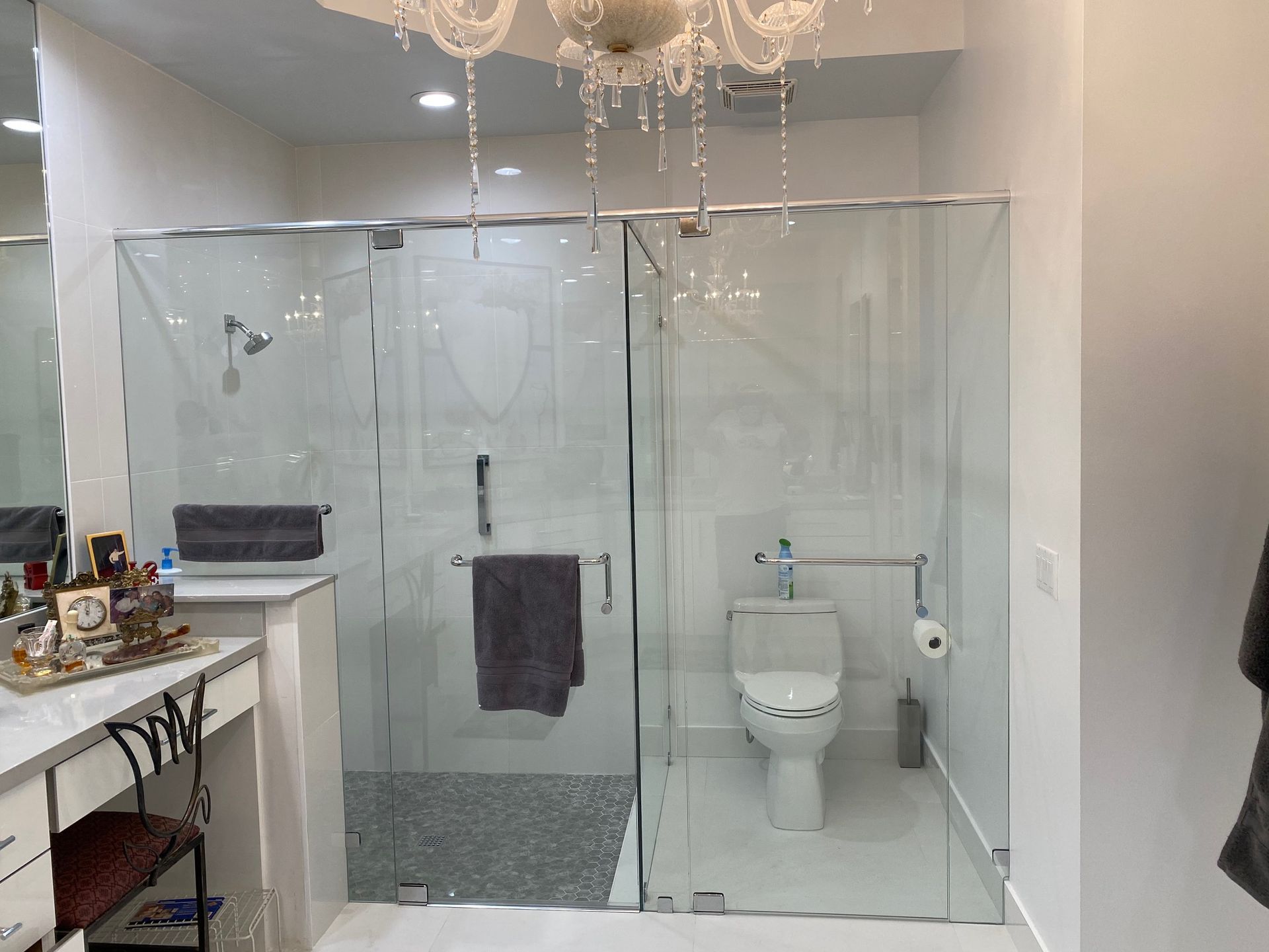 Bathroom with clear glass shower enclosure and toilet. Vanity with accessories visible.