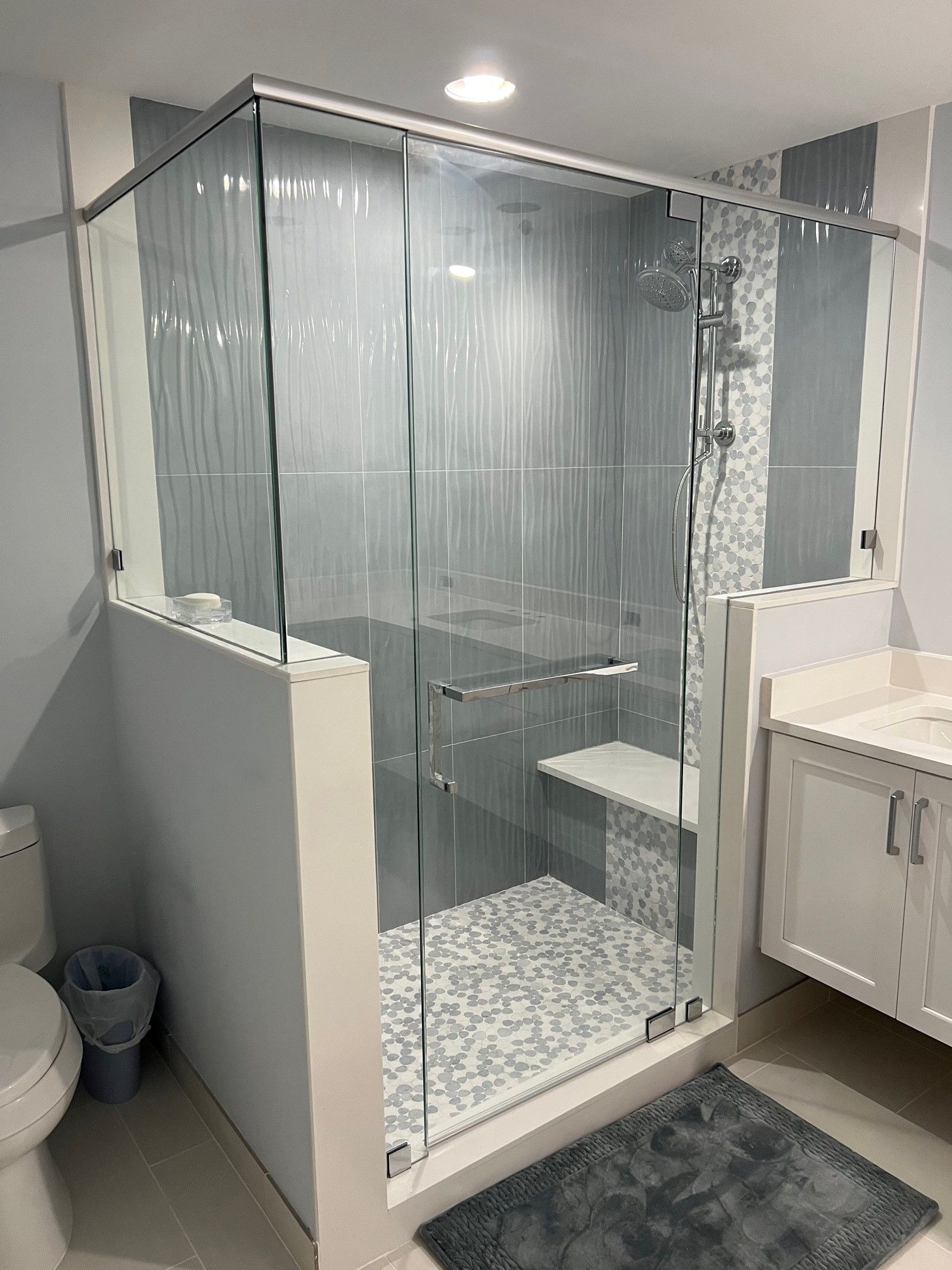 Modern bathroom with glass shower enclosure, mosaic tile floor, white vanity.