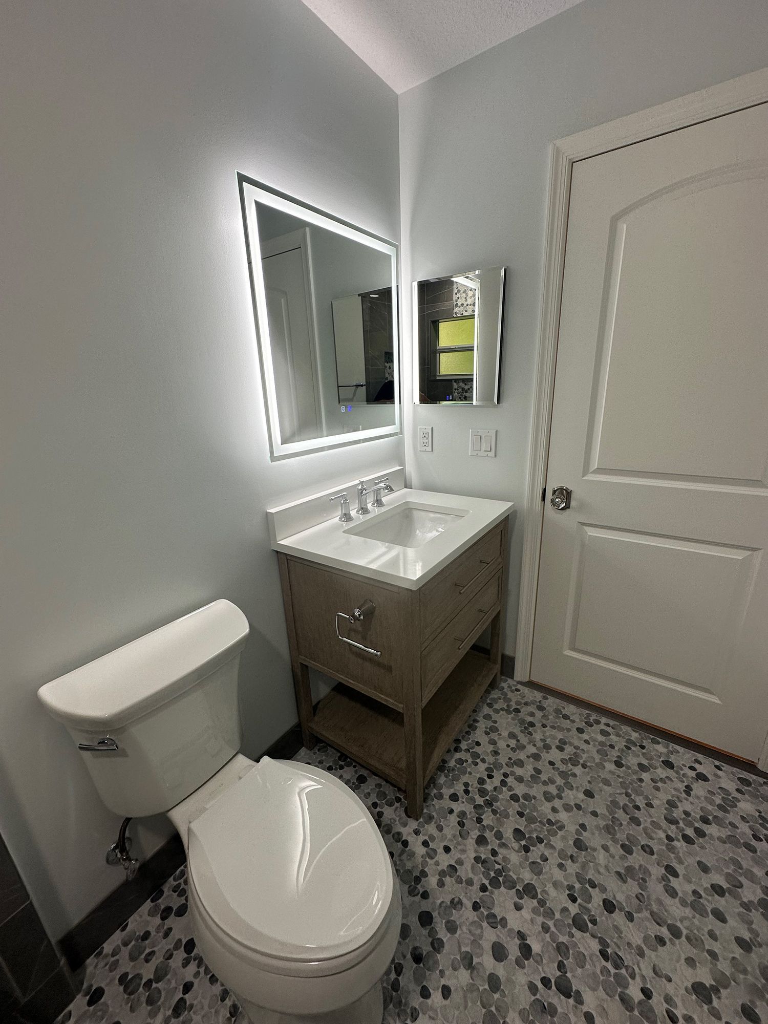 Bathroom with toilet, vanity, mirror with LED lights, and patterned floor.