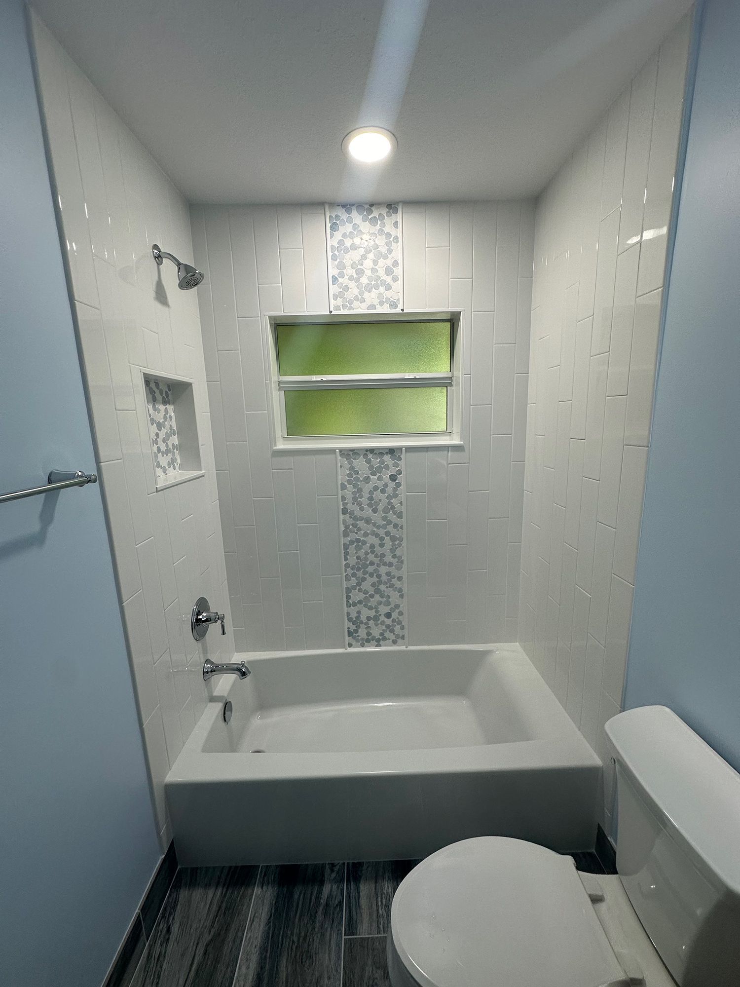 Bathroom with white and blue tile, bathtub, toilet, and a small window.