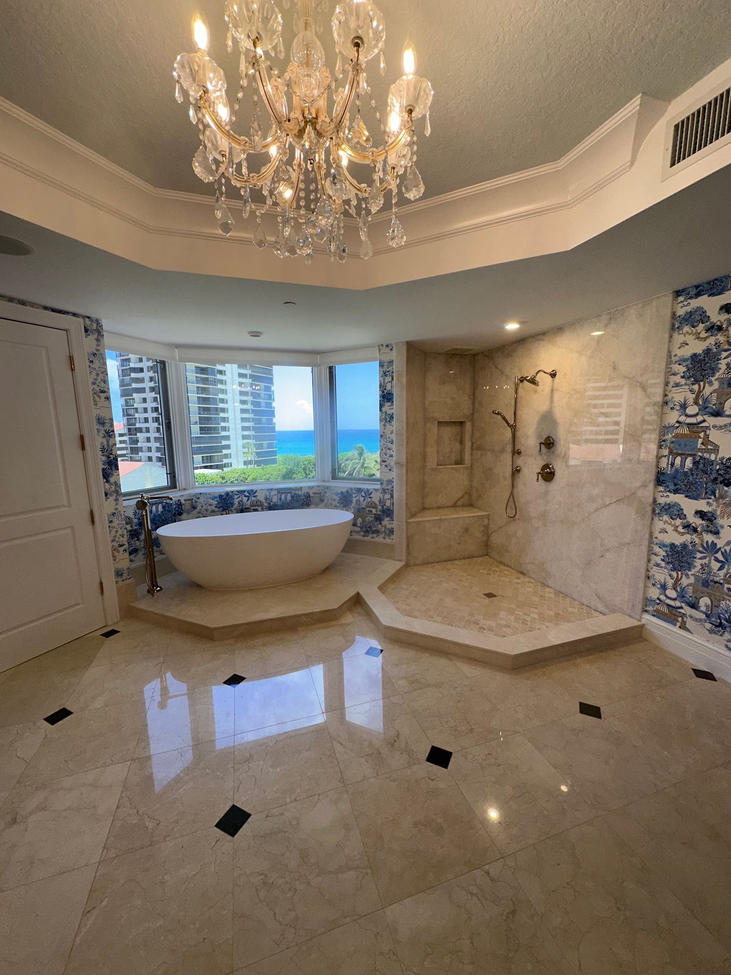 Luxurious bathroom with soaking tub, shower, ocean view, chandelier, and patterned walls.