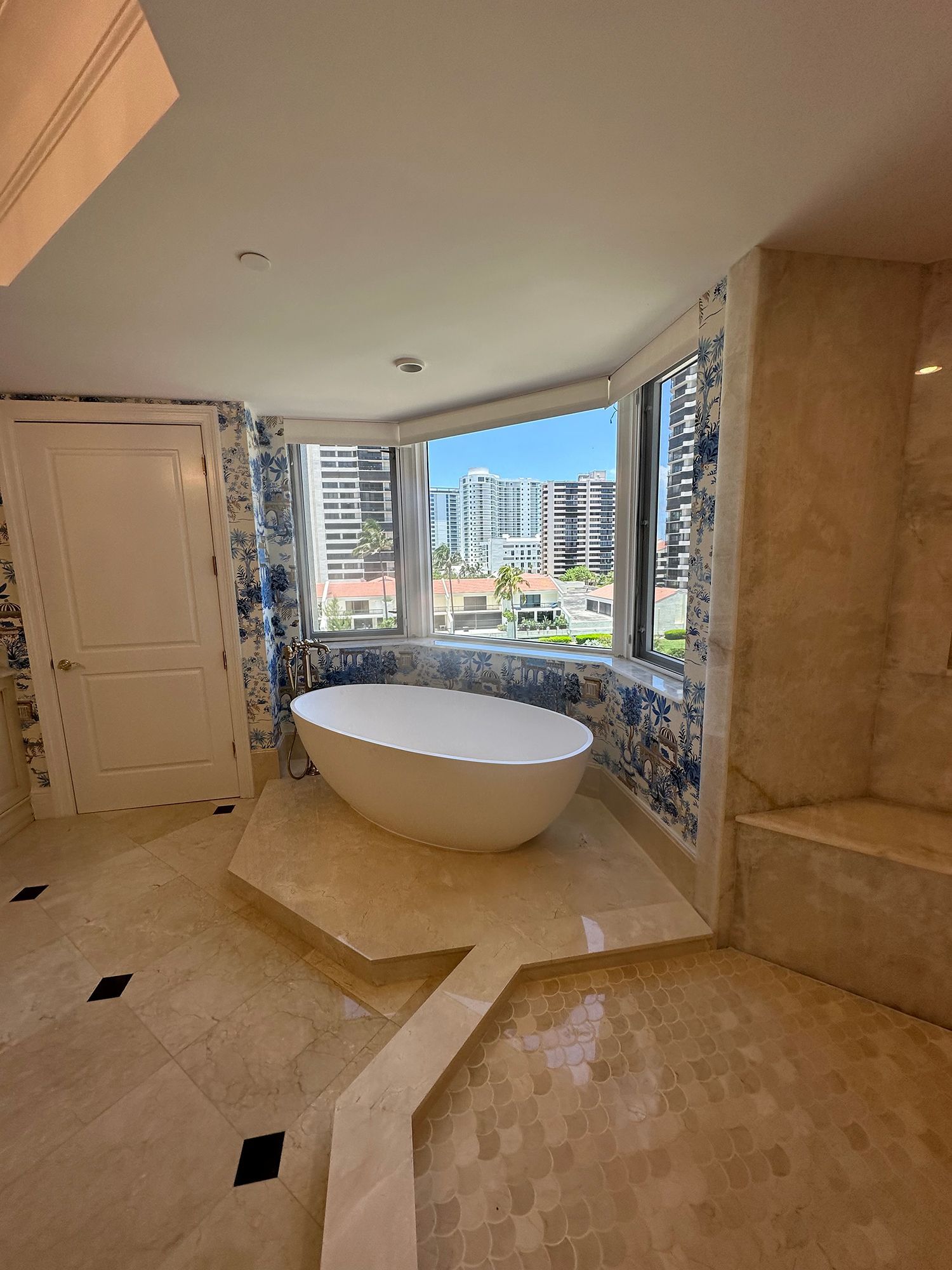 Elegant bathroom with a white freestanding tub in front of a large window, city view.