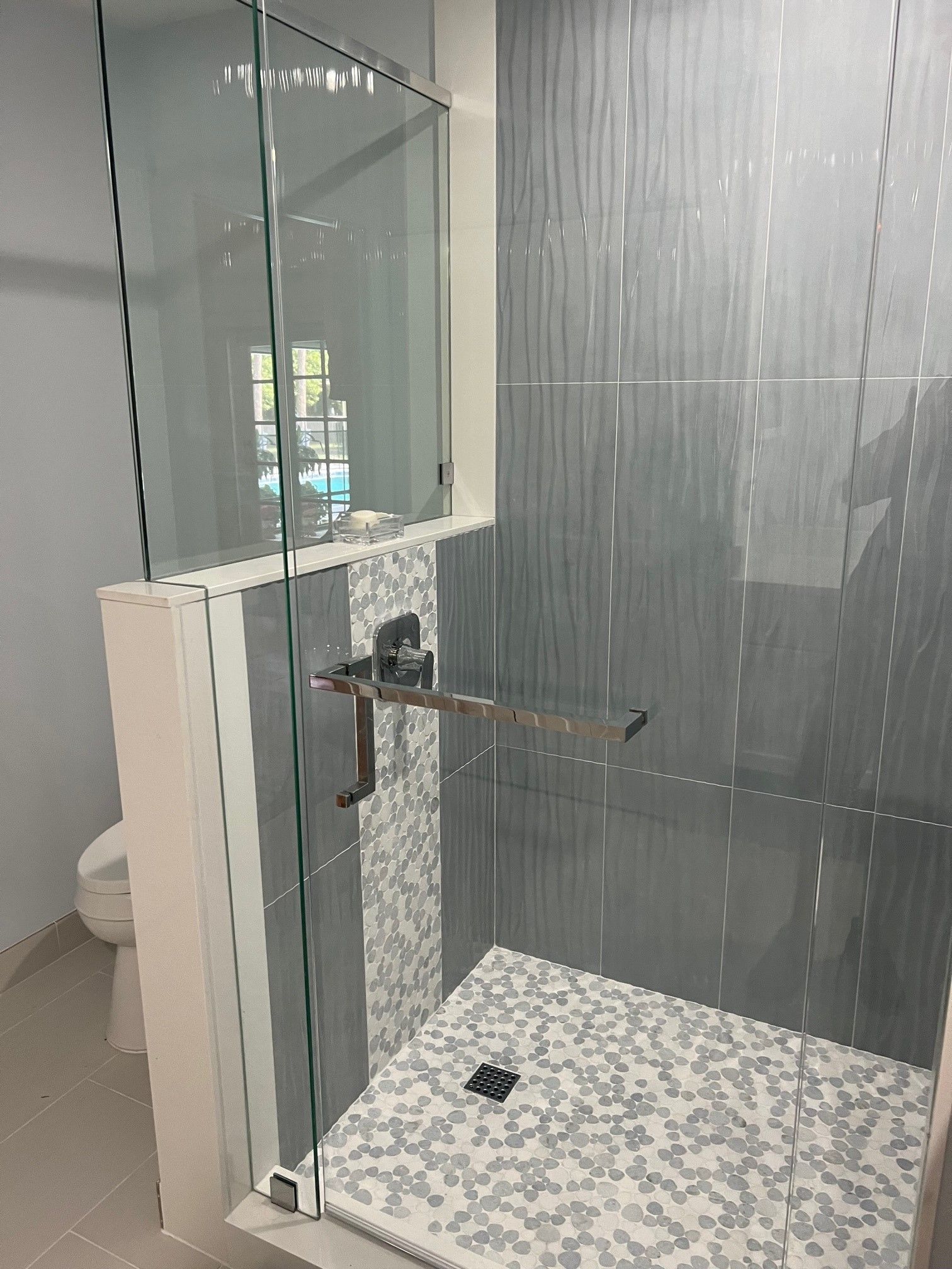 A modern shower with glass doors and blue-gray tiled walls and floor. A silver grab bar is mounted on the glass.