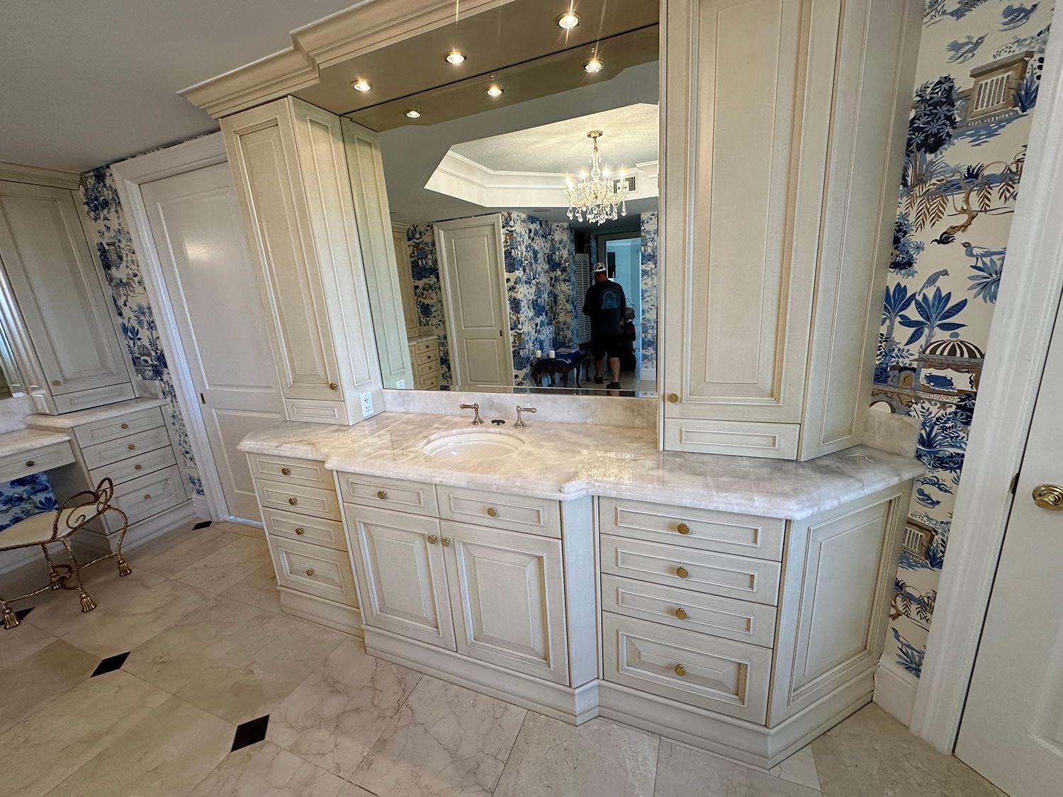 Bathroom with white cabinetry, marble countertop, blue patterned wallpaper, and a large mirror.