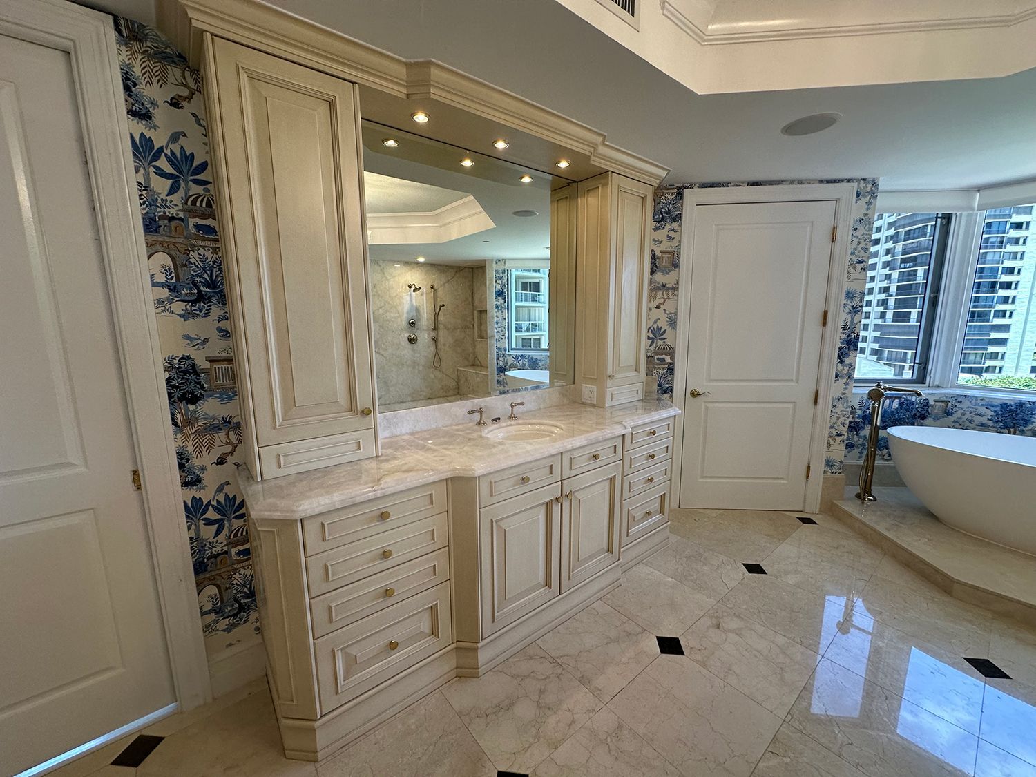 Luxurious bathroom with cream cabinets, large mirror, floral wallpaper, and a freestanding tub.