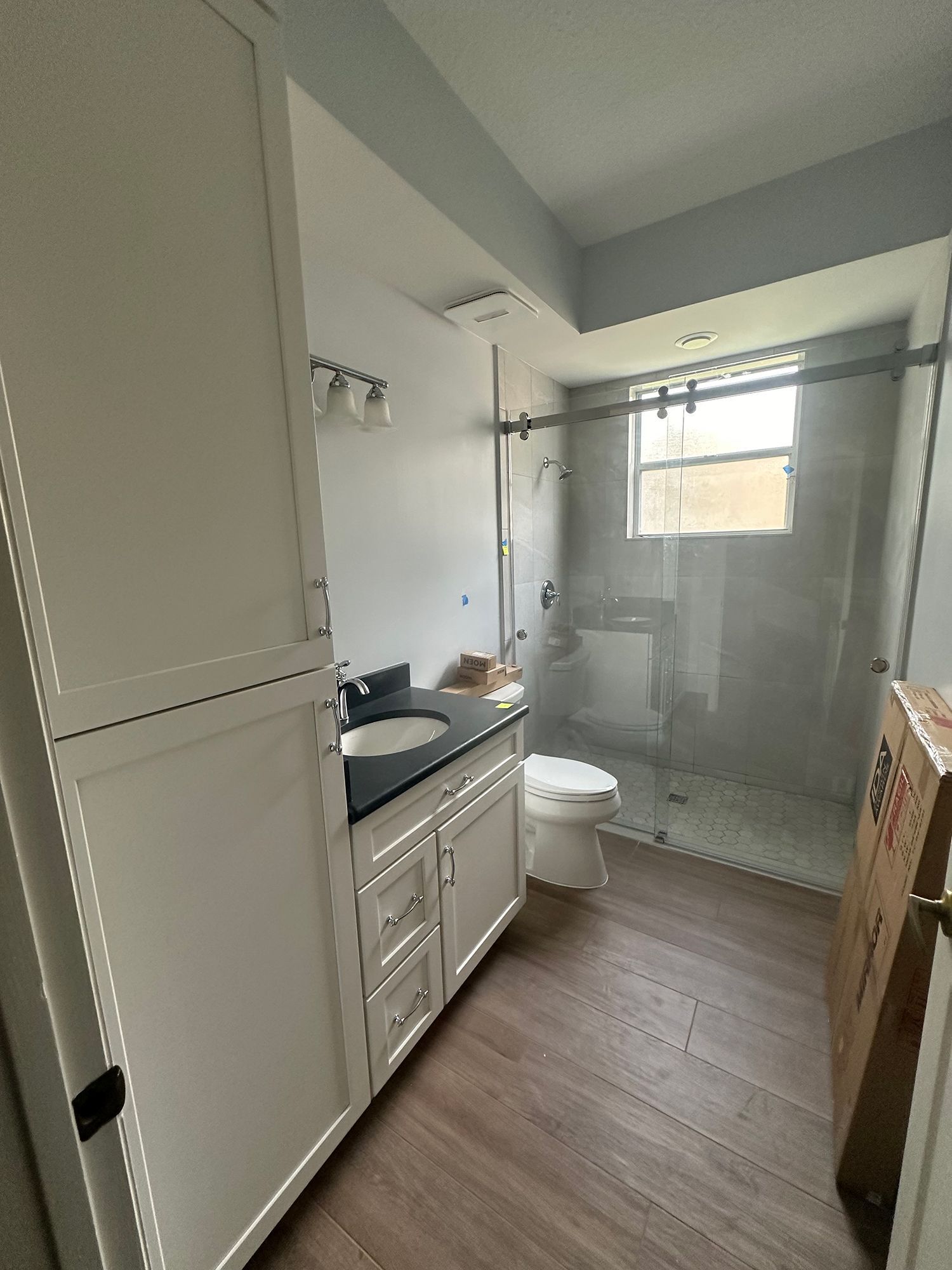 Bathroom with white cabinets, black countertop, glass shower, and wooden floor.