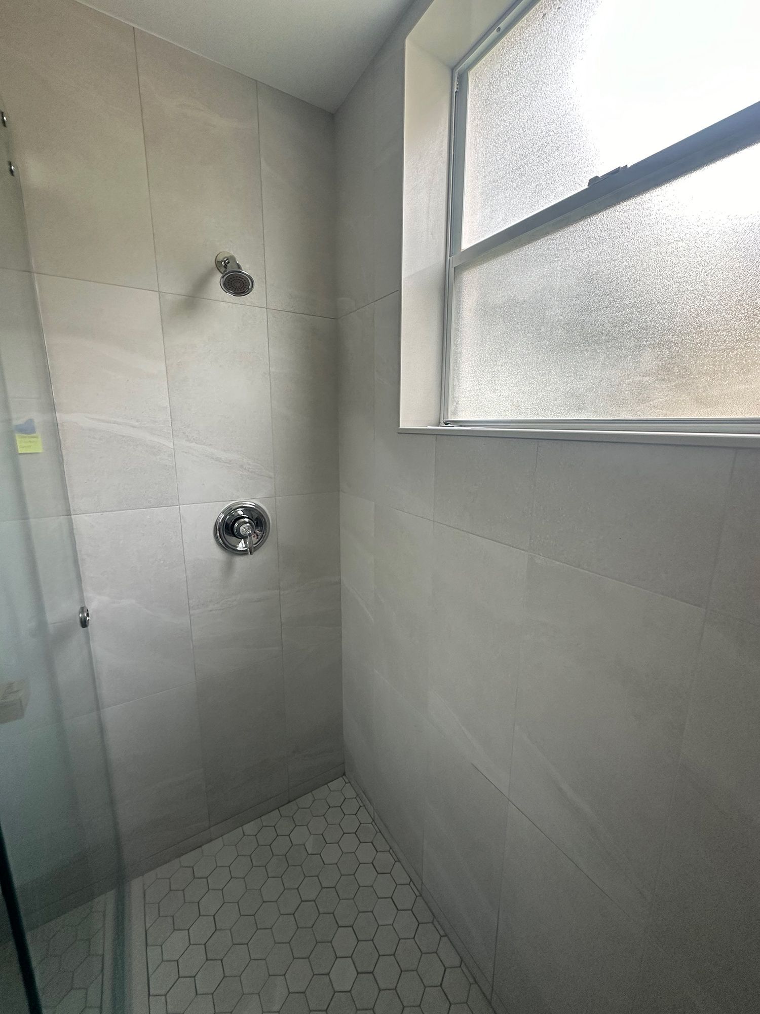 Shower stall with gray tile walls, chrome fixtures, and a frosted window.