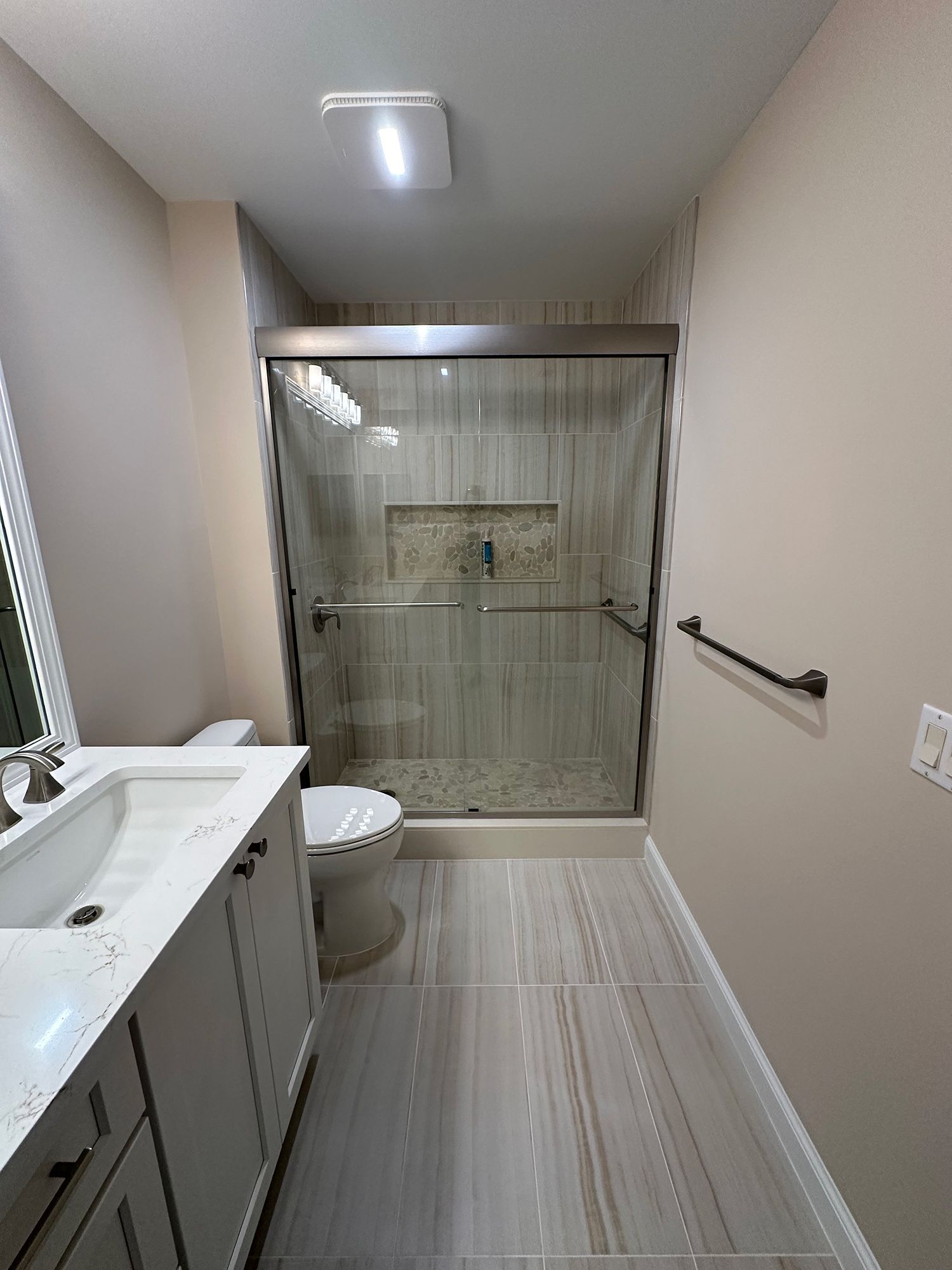 Bathroom with a walk-in shower, white vanity, toilet, and light-colored tile floor and walls.