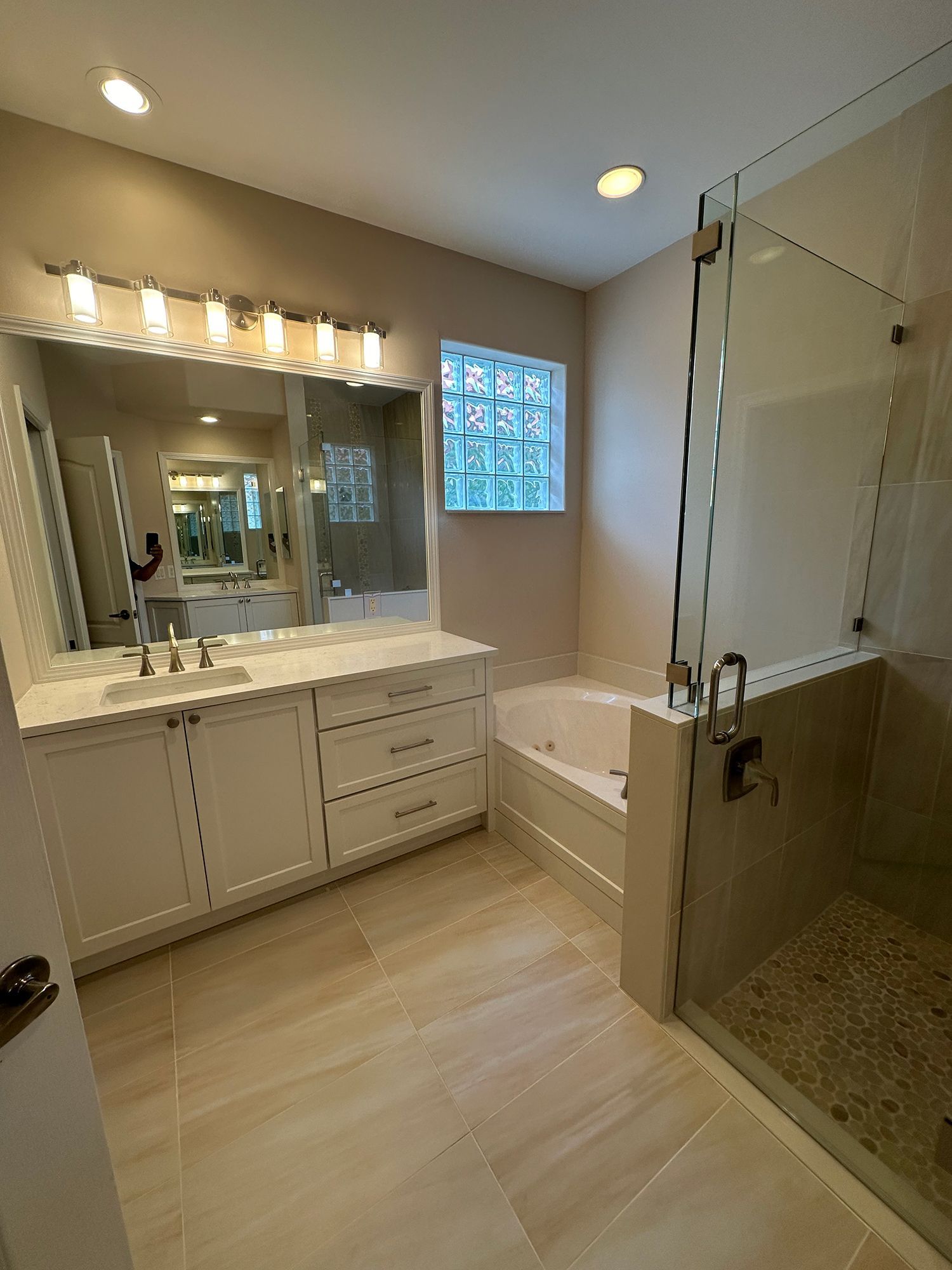Bathroom with a vanity, bathtub, shower, and a glass-block window. Beige walls and tiled floor.