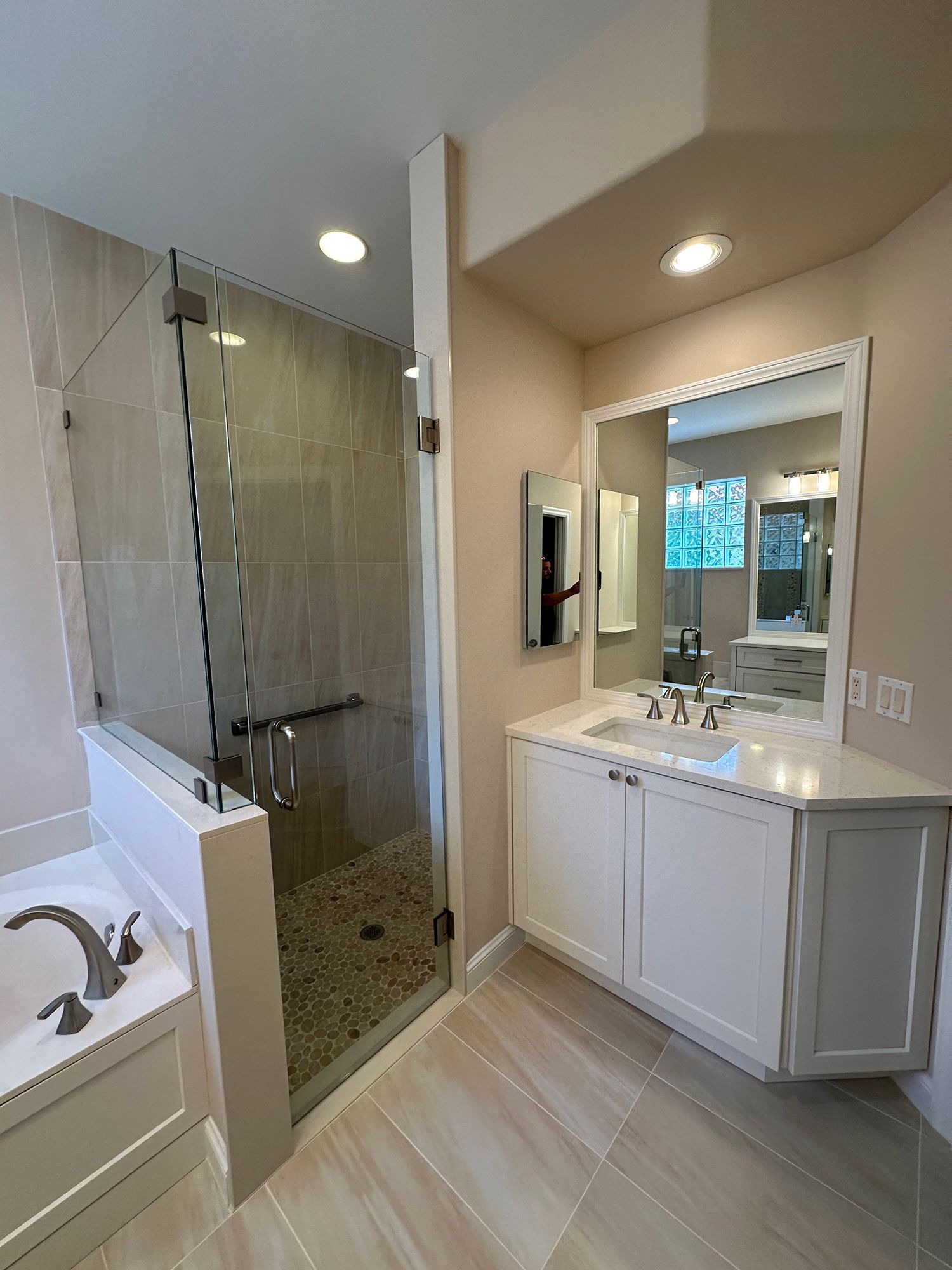 Modern bathroom with a glass shower, white vanity, and neutral-toned tiles.