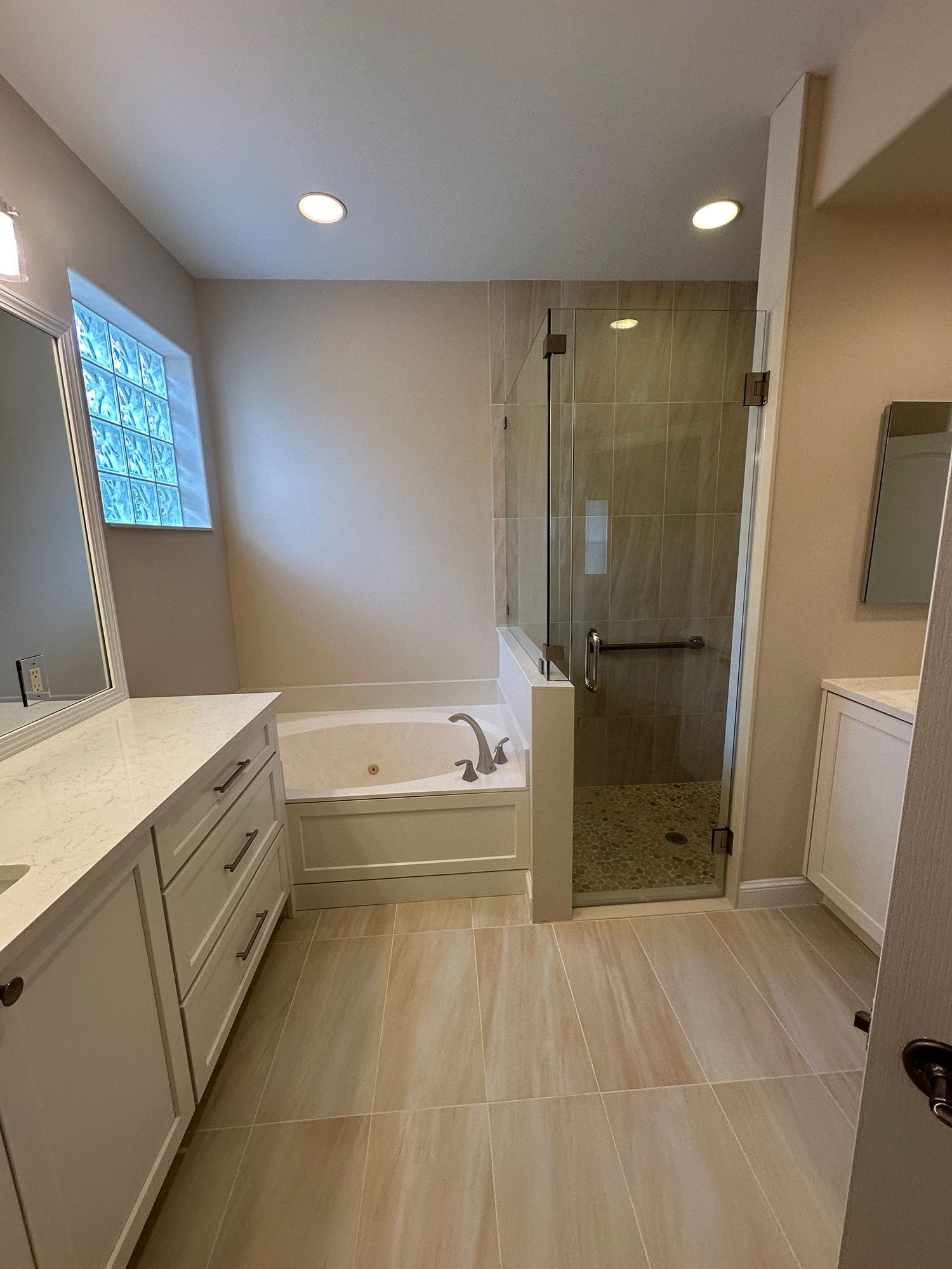 Bathroom with white vanity, tub, and glass shower. Beige walls and tile flooring.