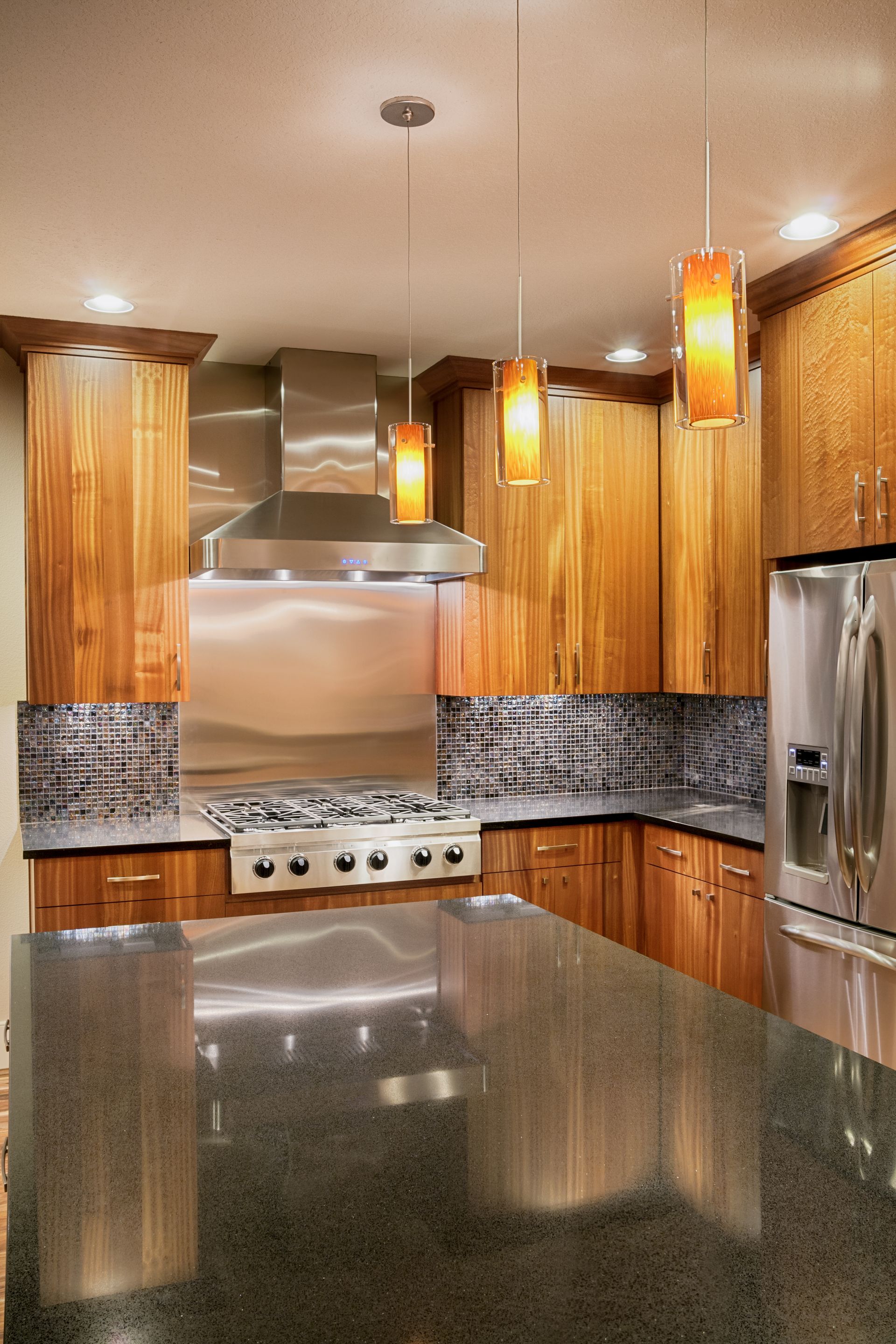 Modern kitchen with wooden cabinets, stainless steel appliances, granite island, and pendant lights.