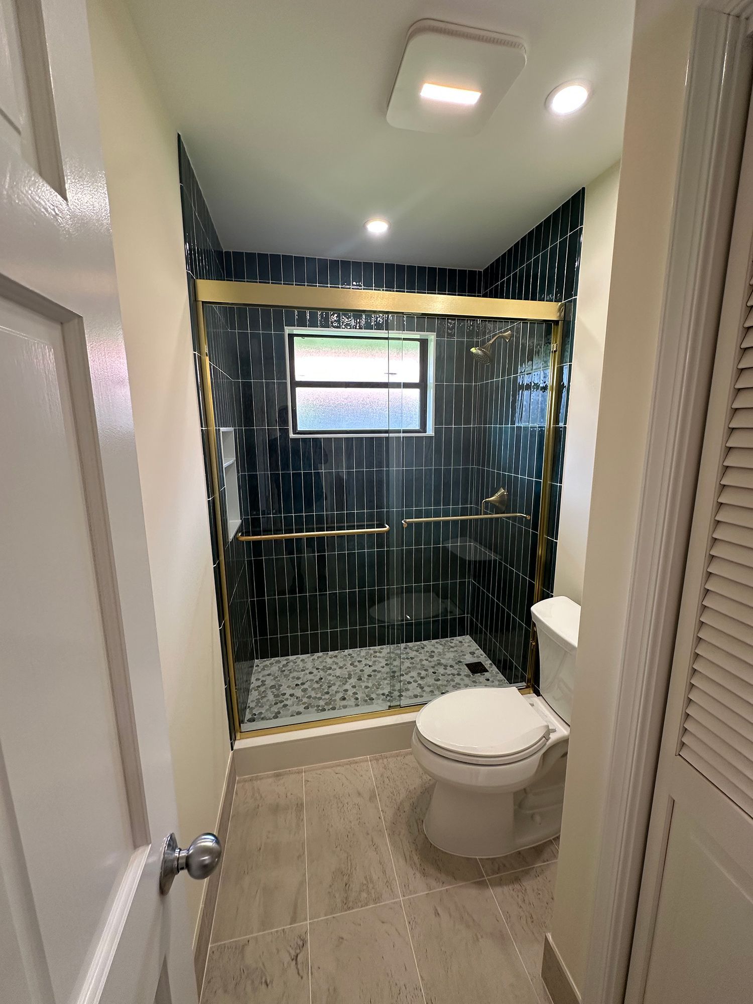 Newly renovated bathroom with black tiled shower, gold fixtures, and a white toilet.