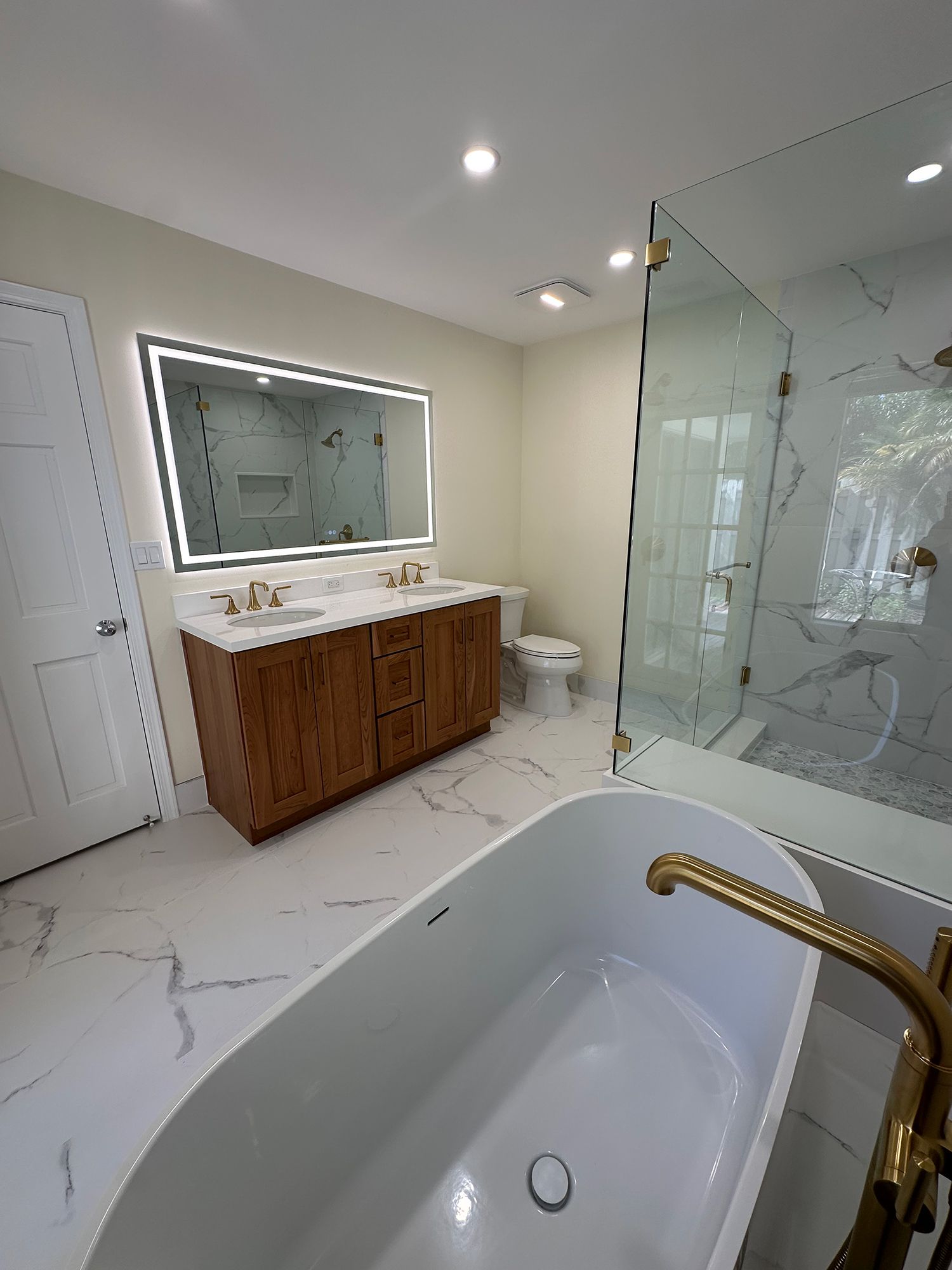 Bathroom with a wood vanity, large mirror, glass shower, and freestanding tub.