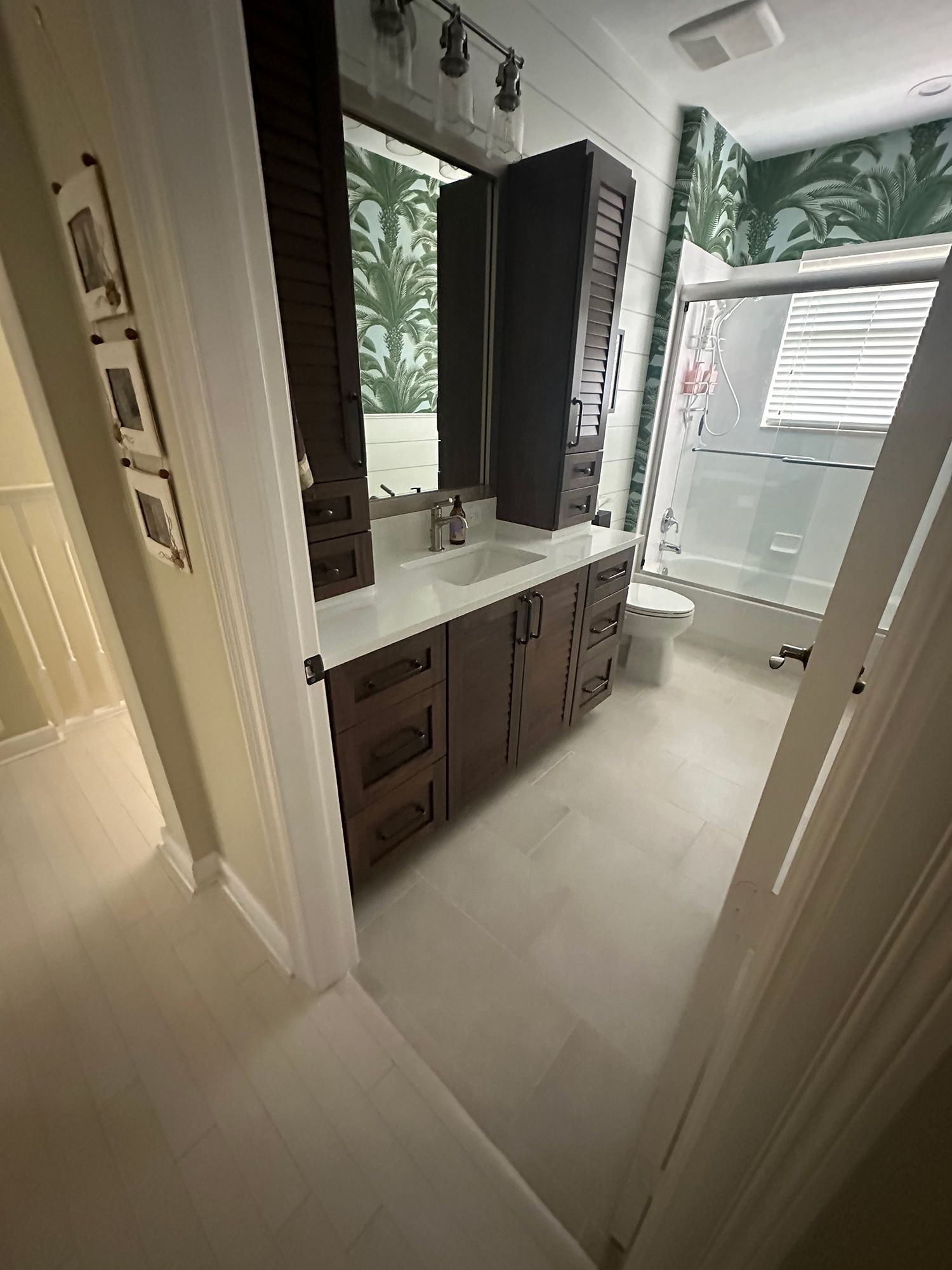 Bathroom with dark wood vanity, white countertop, green palm wallpaper, and a shower/tub.