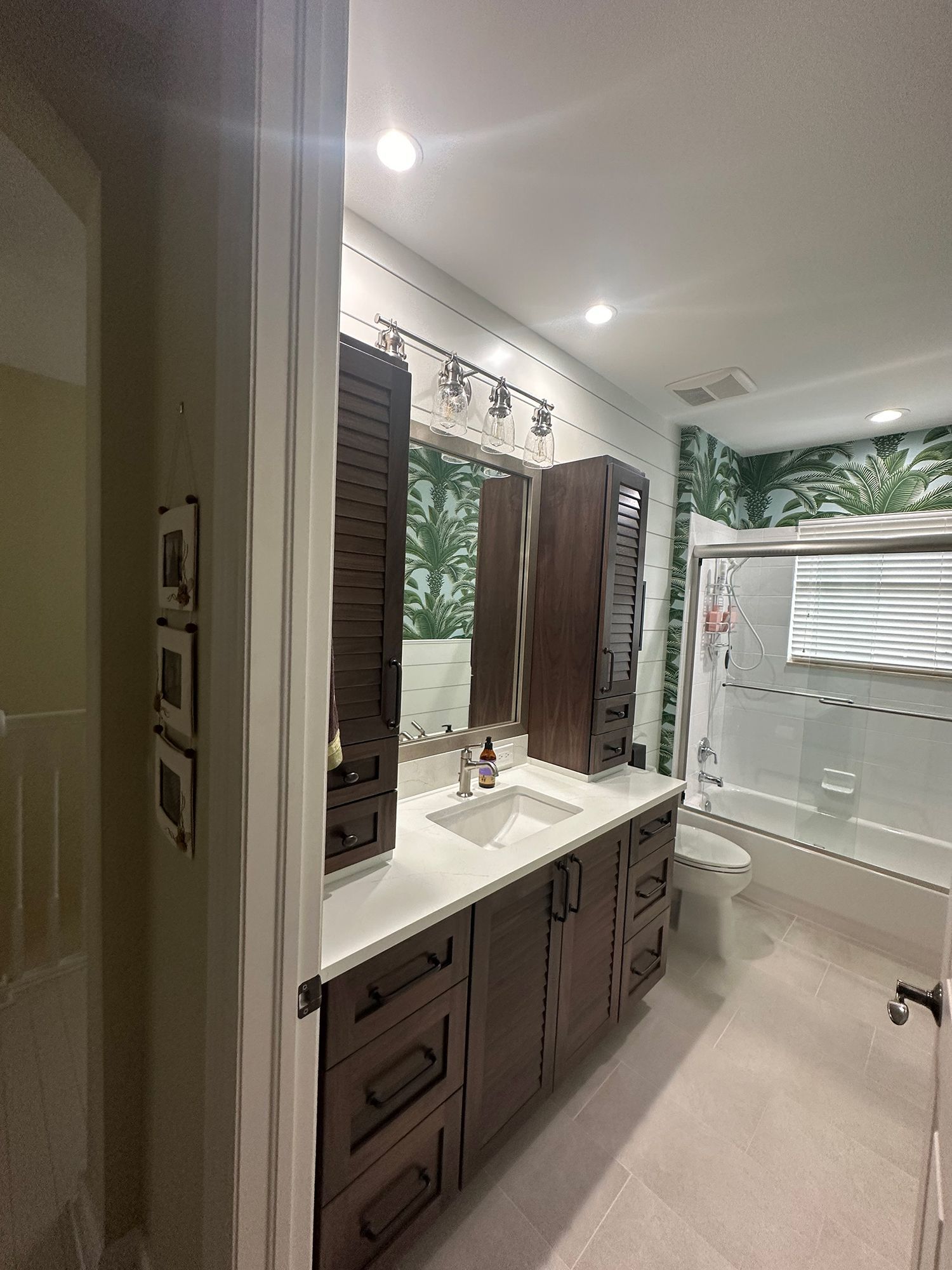 Bathroom with dark wood vanity, white countertop, and patterned wallpaper behind the toilet.
