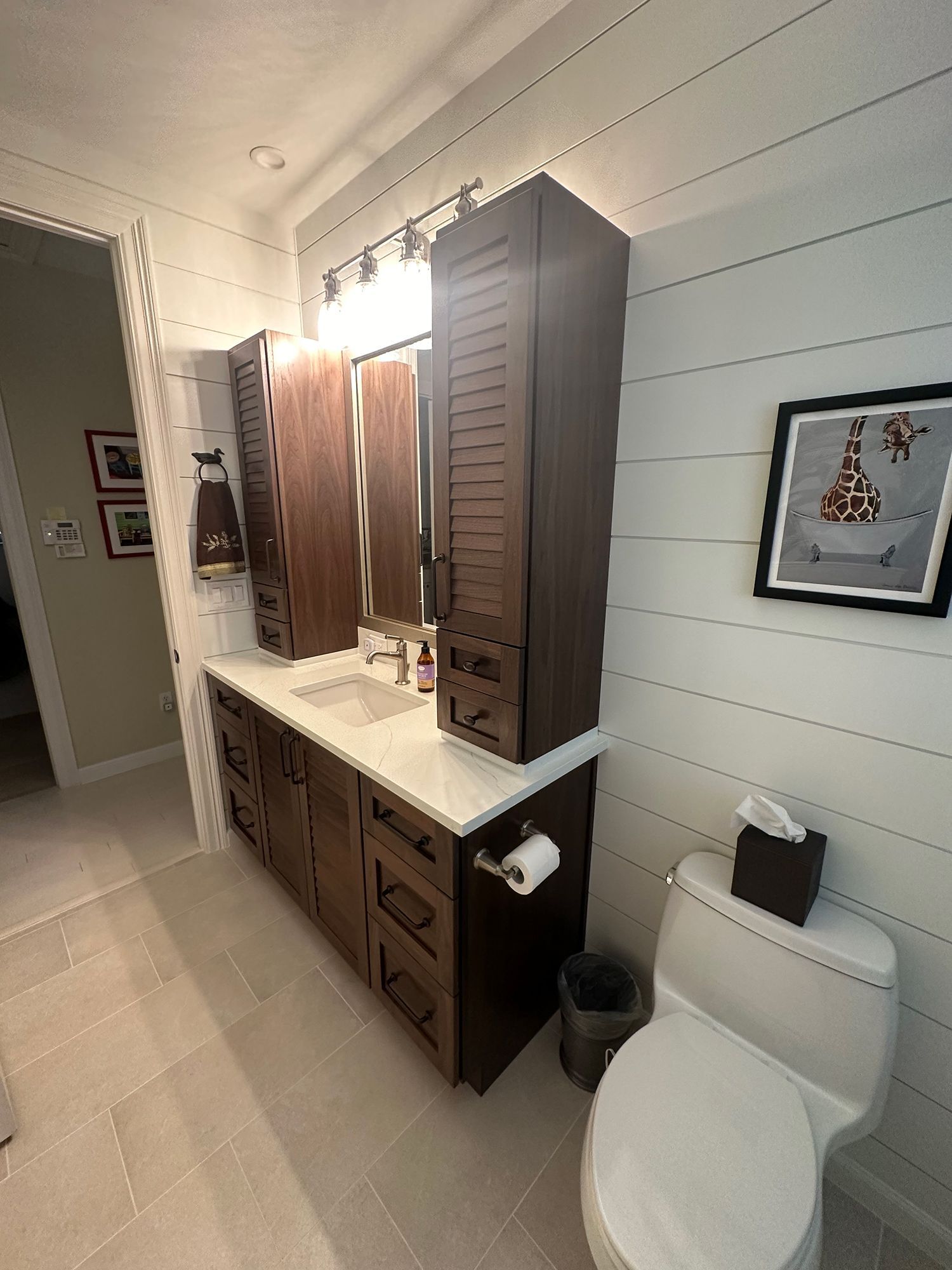Bathroom with dark wood vanity, white countertop, tall cabinets, toilet, and shiplap walls.