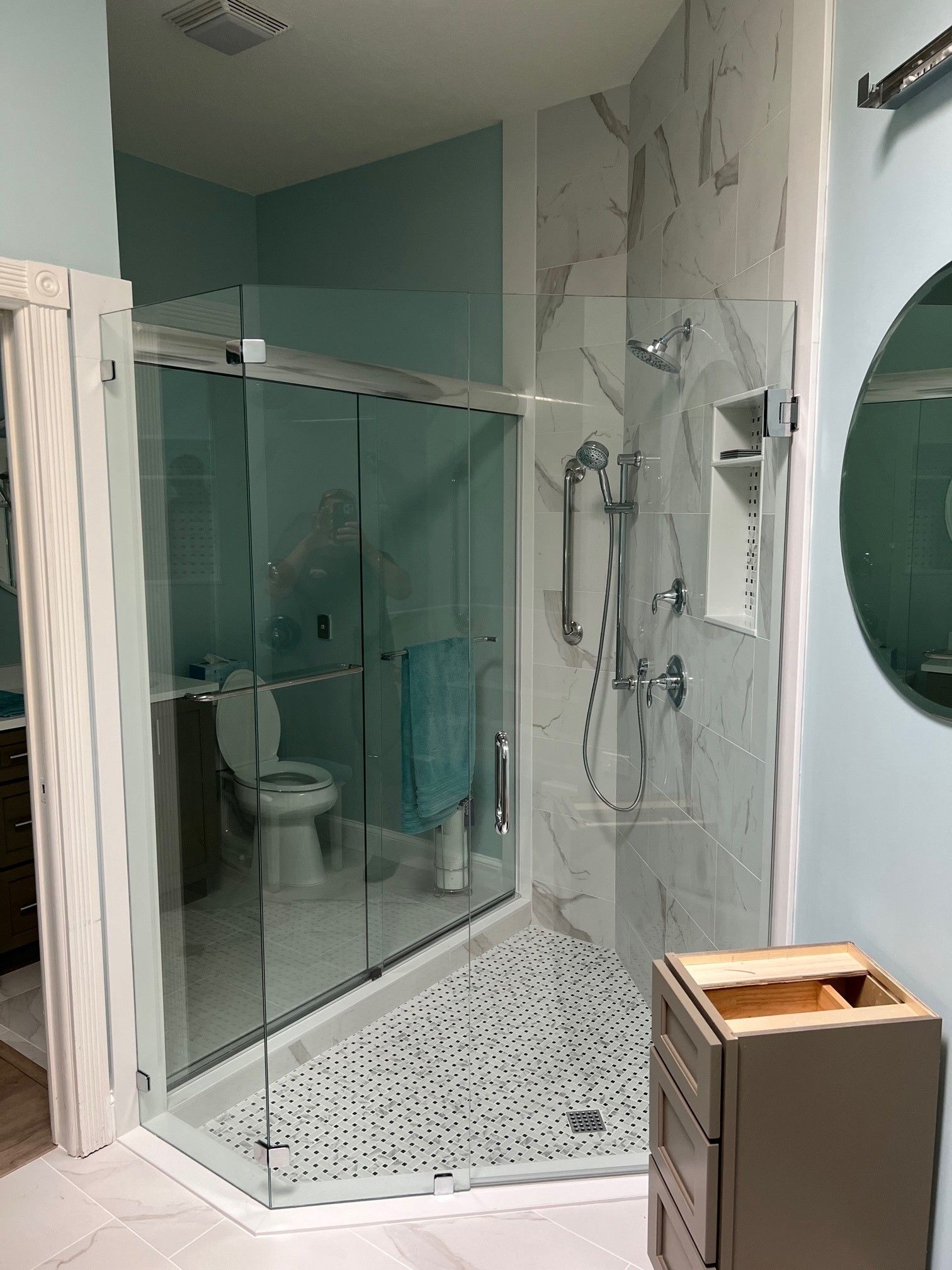 Modern bathroom with glass shower, blue walls, white and gray tile, toilet, and empty vanity.