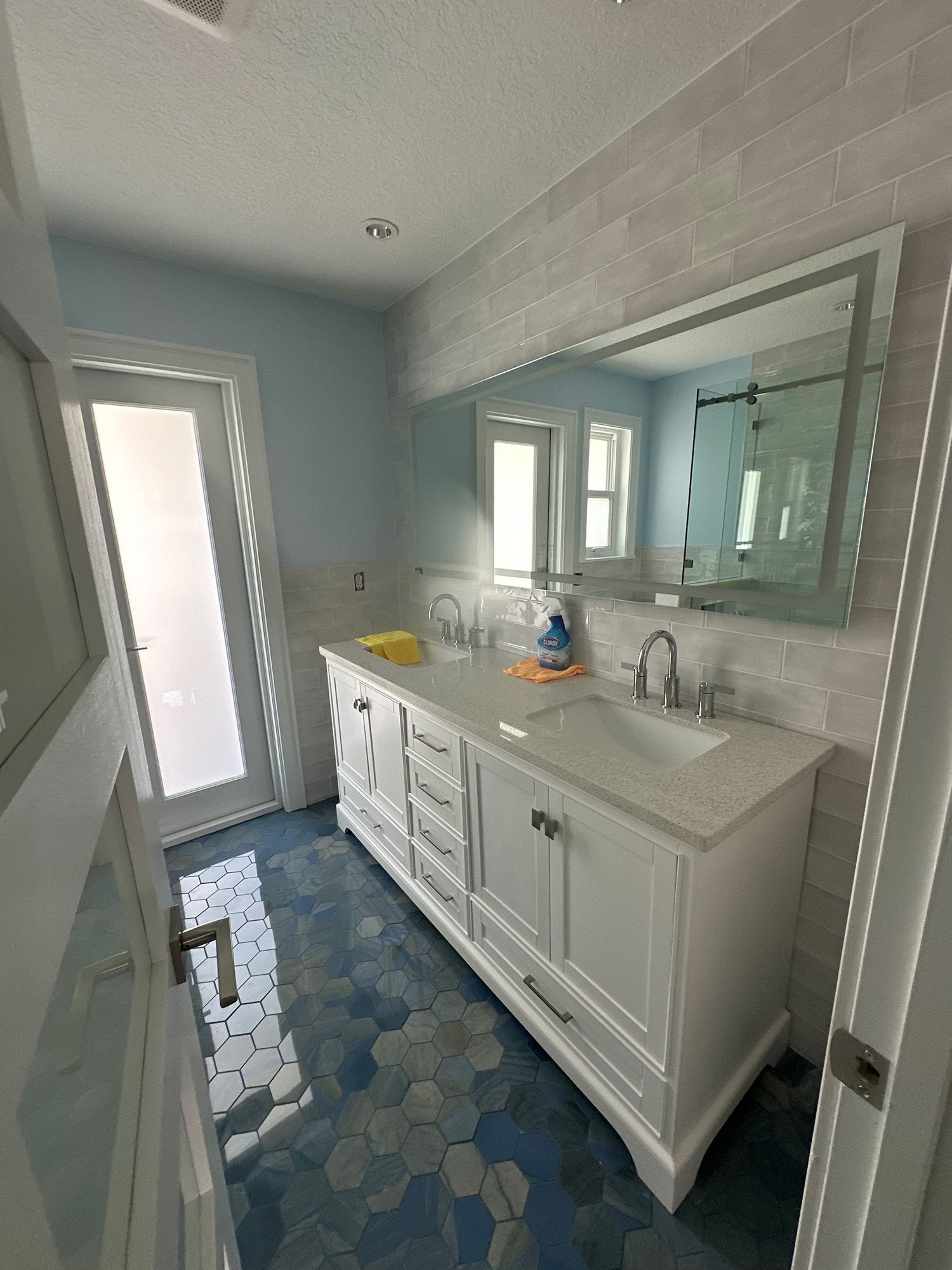 Bathroom with white vanity, blue and white hexagonal tile floor, frosted glass door.