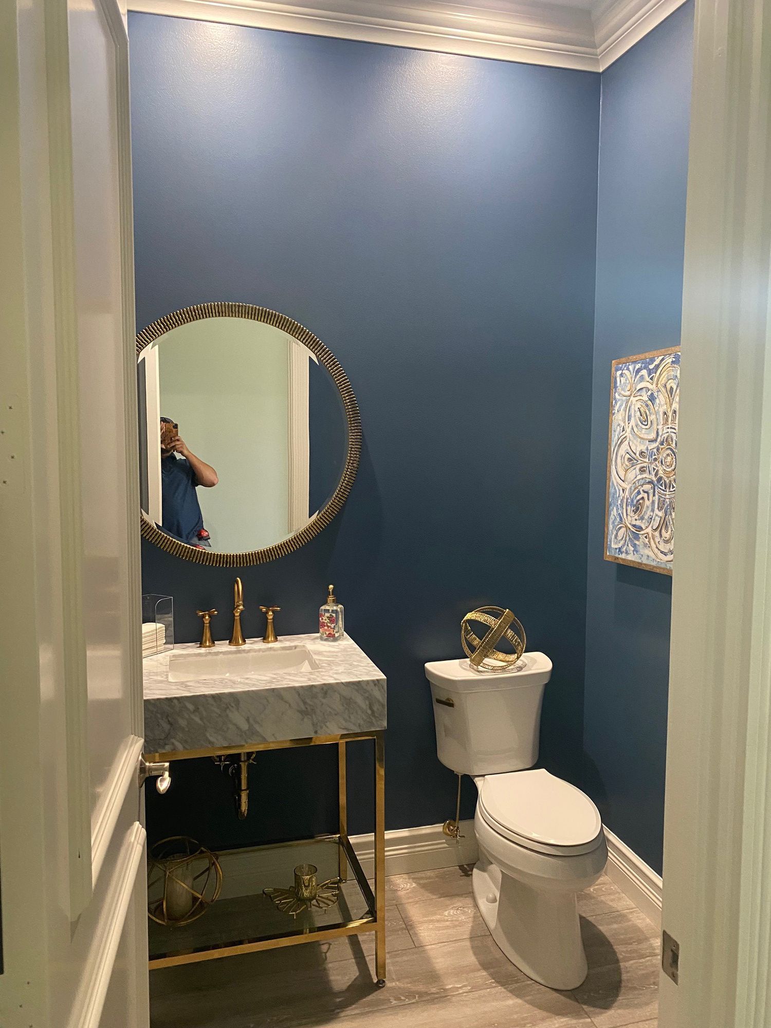 Small bathroom with blue walls, gold accents, marble sink, and round mirror.