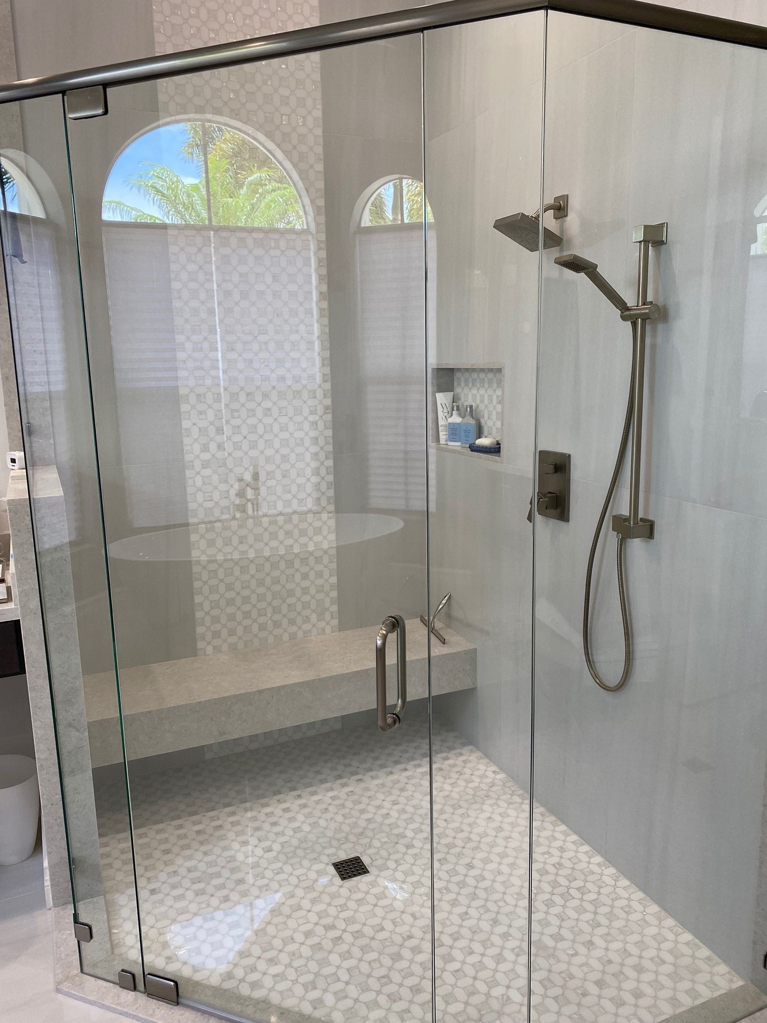 Modern bathroom shower with clear glass doors, light-colored tile, and built-in bench.