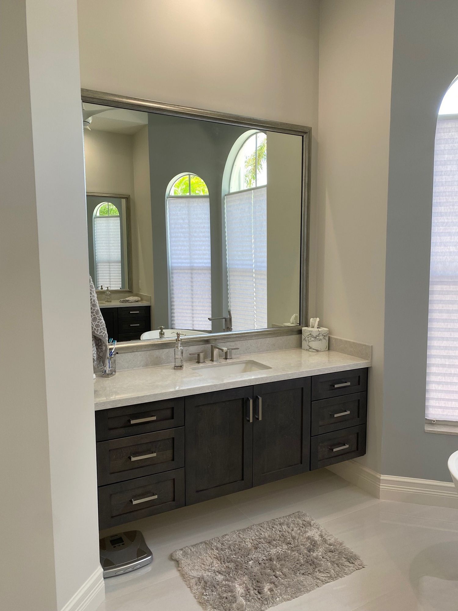 Bathroom with floating dark gray vanity, large mirror, and two arched windows.