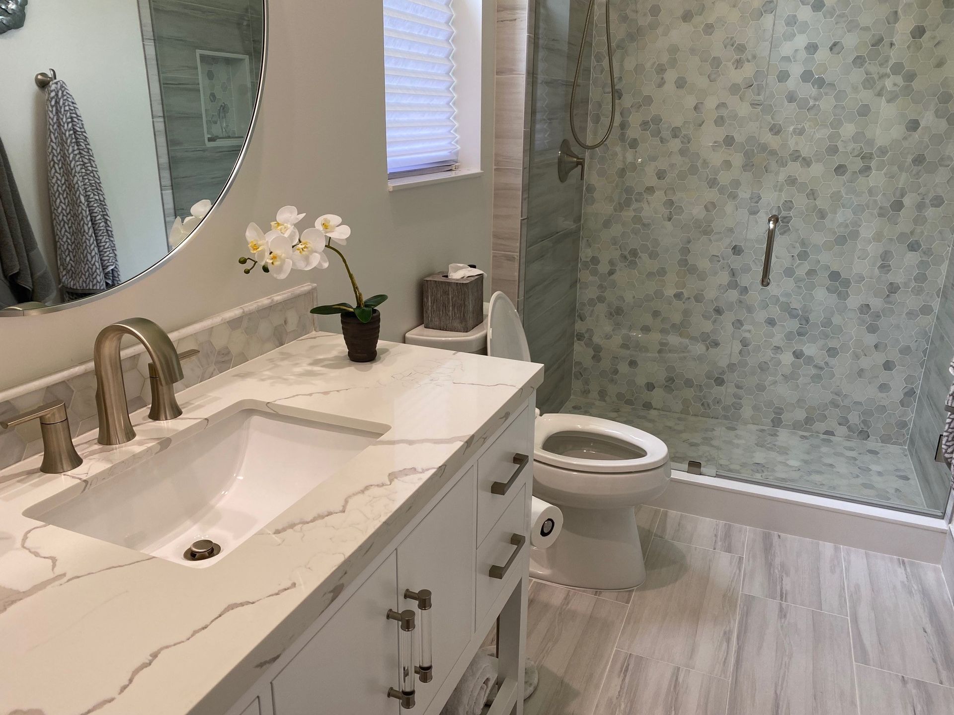Modern bathroom with white vanity, sink, toilet, and shower with patterned tile.