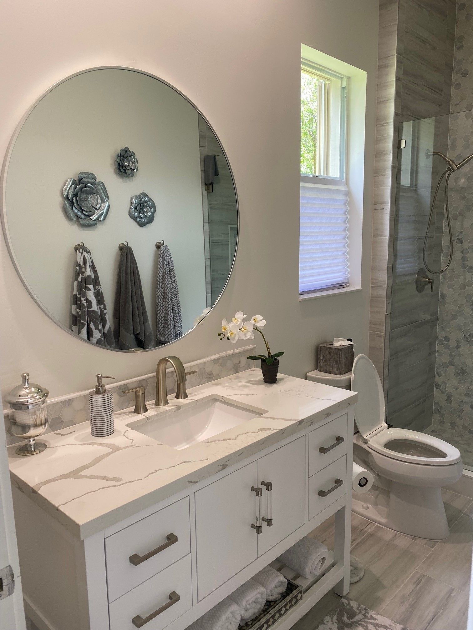 Bathroom with white vanity, round mirror, marble countertop, and tiled shower.