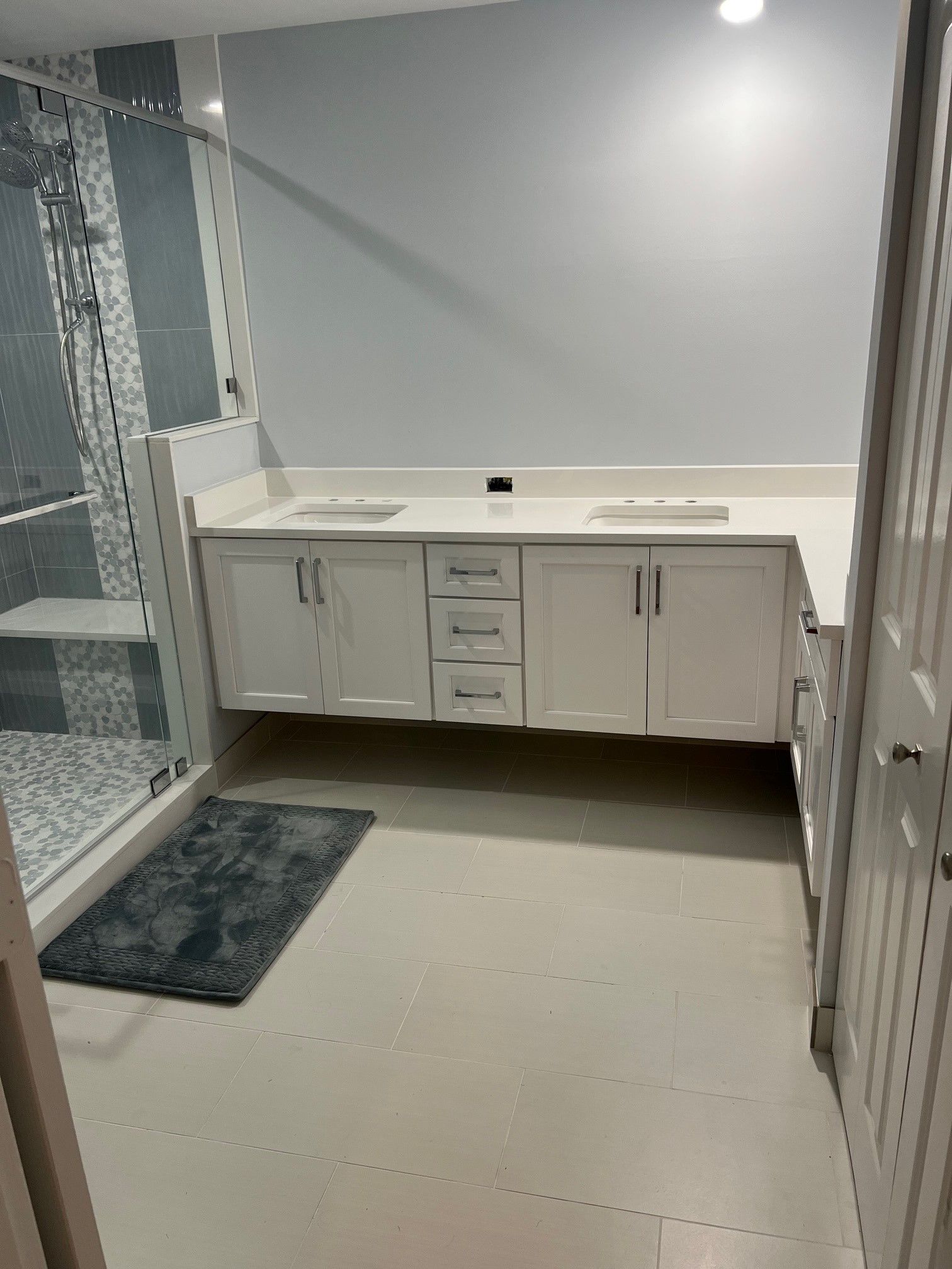 Bathroom with white cabinets, shower, and a bath mat.