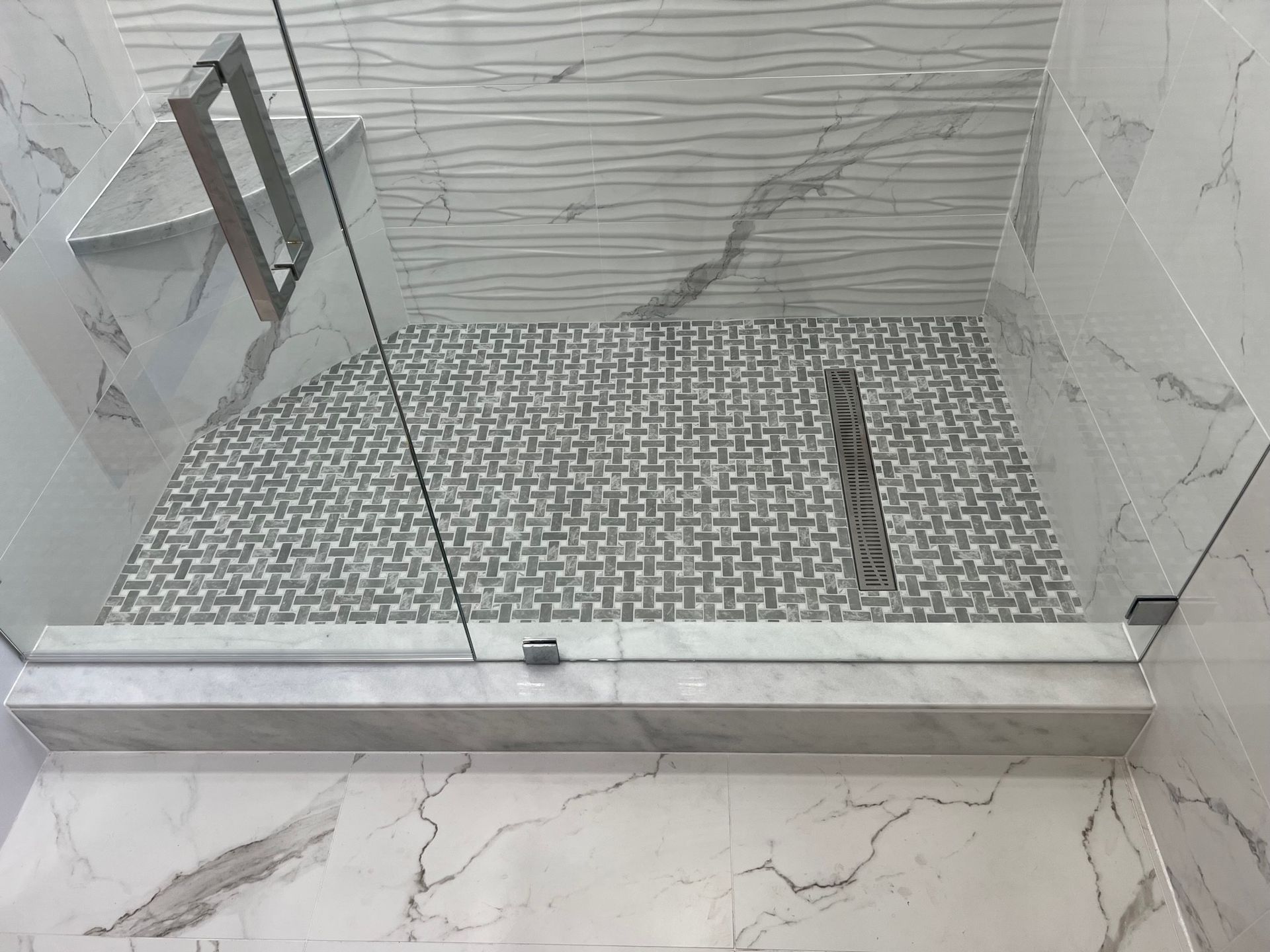 Modern shower with patterned floor tiles, white marble walls, and glass doors.