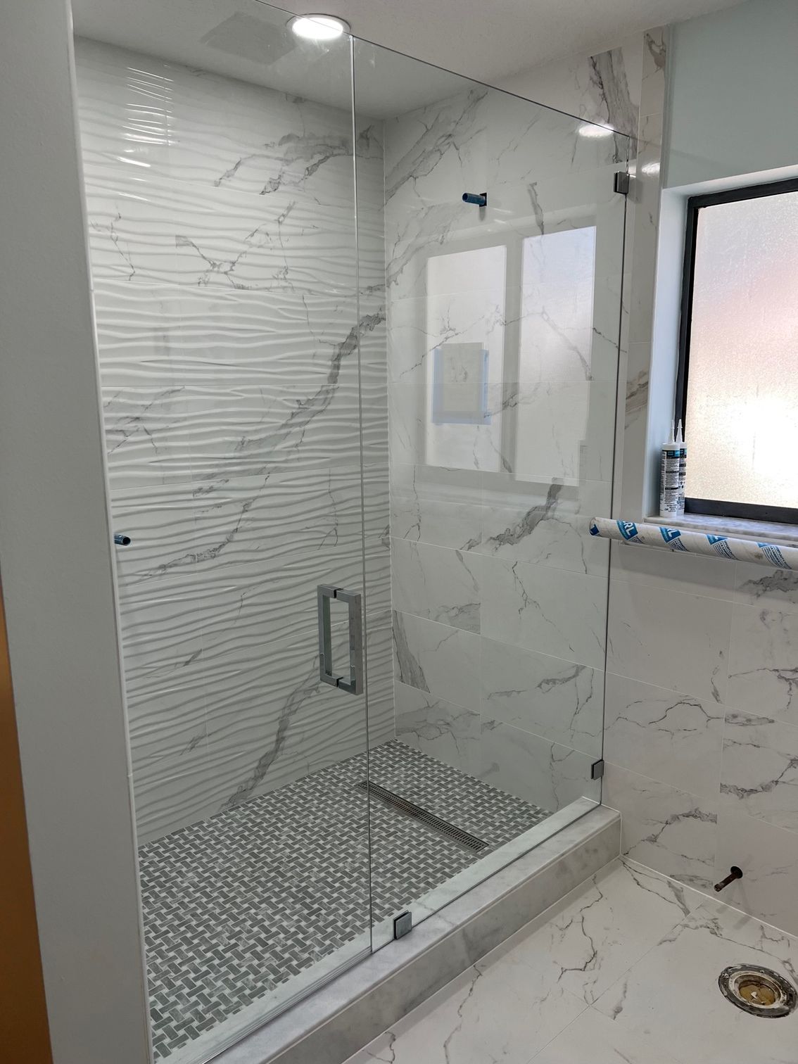 Modern shower with clear glass enclosure and marble tile walls.