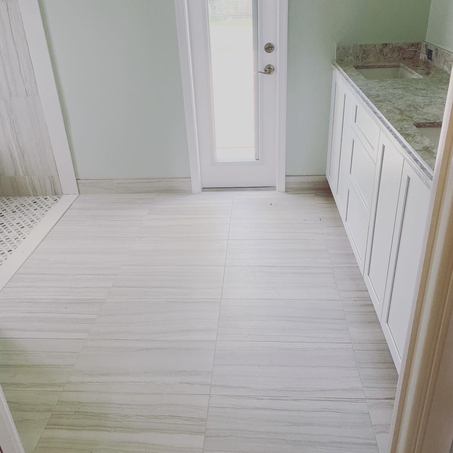 Bathroom with white tile floor, white cabinets, and a door. Light green walls, granite countertop.