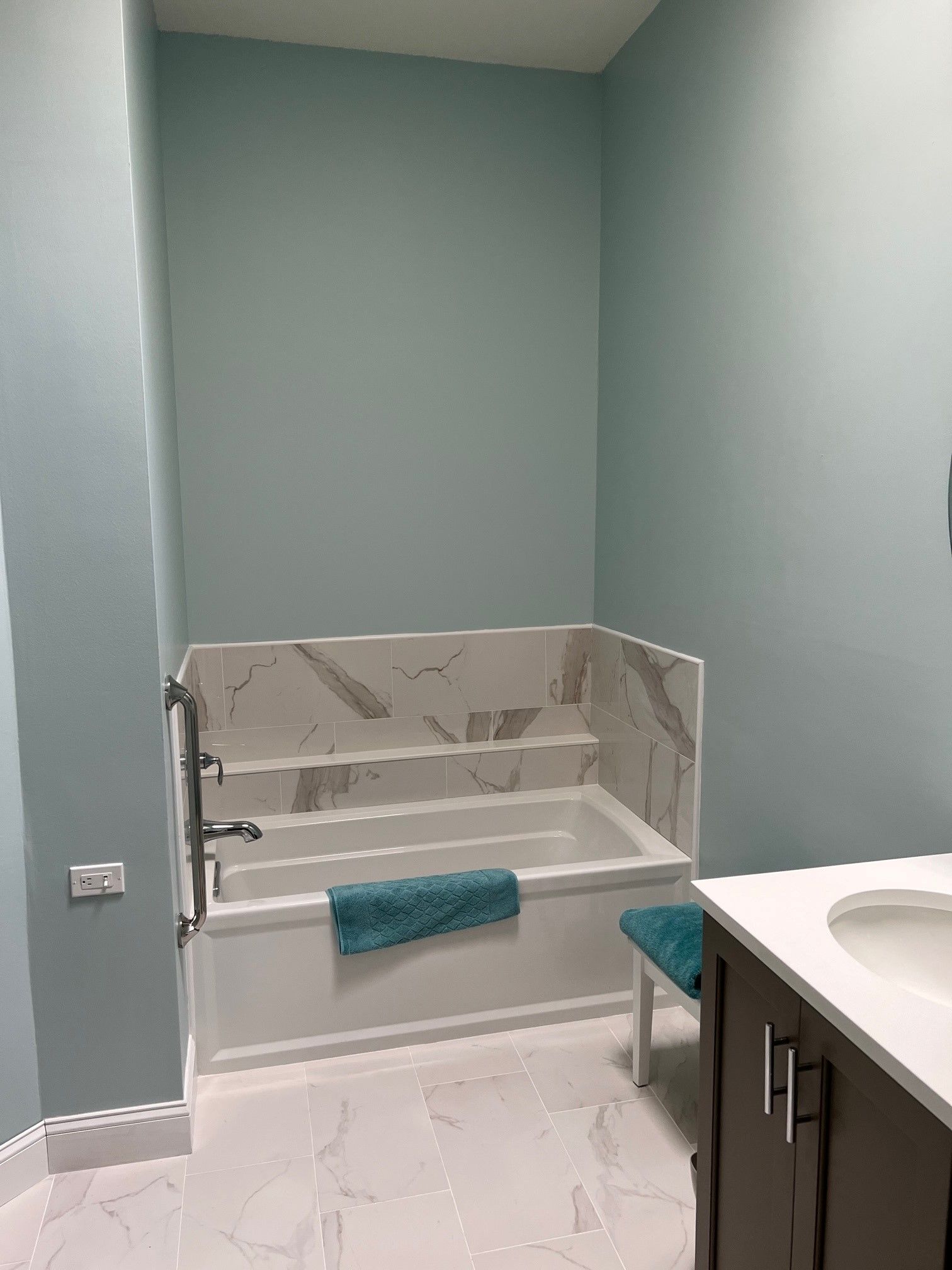 Bathroom with a white bathtub, marble backsplash, and turquoise towel; walls are painted light blue.