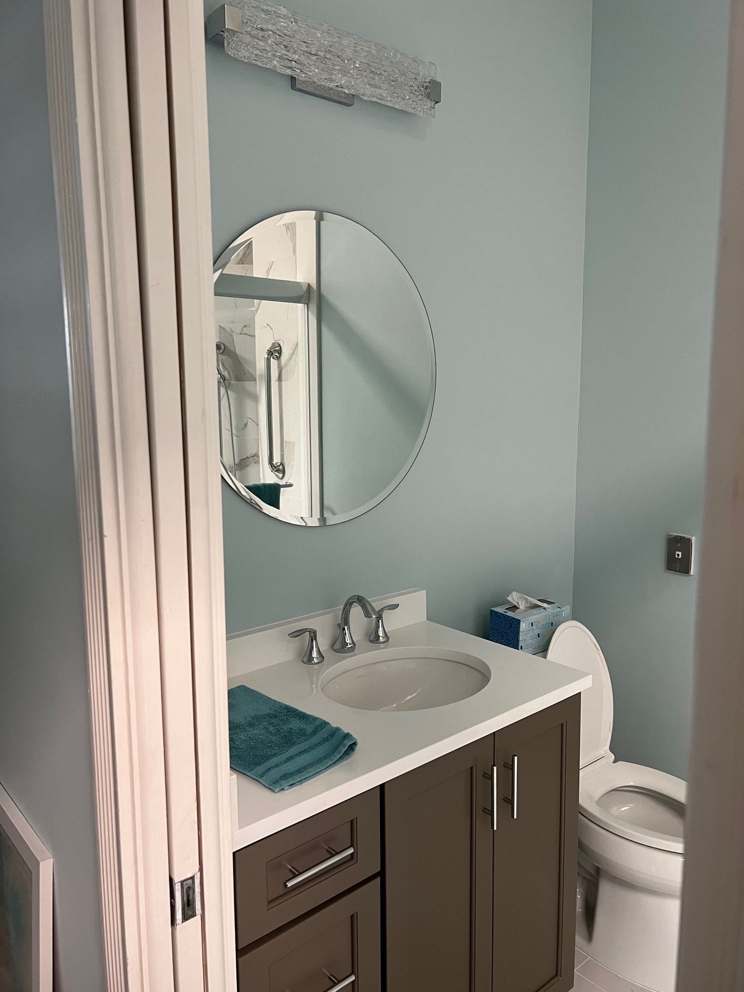 Bathroom with blue walls, round mirror above a sink with a brown cabinet, and a white toilet.