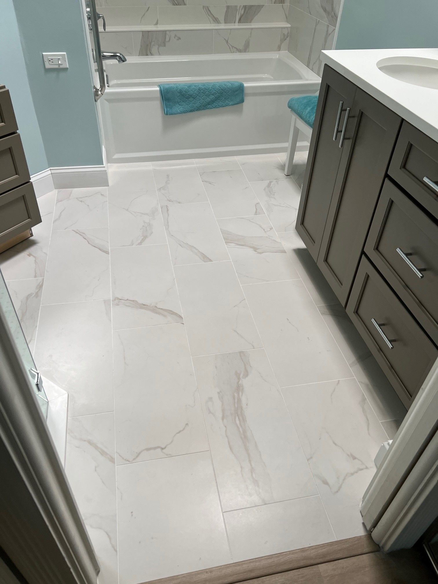 Bathroom with white marbled floor tiles, tub, vanity, and a blue accent wall.