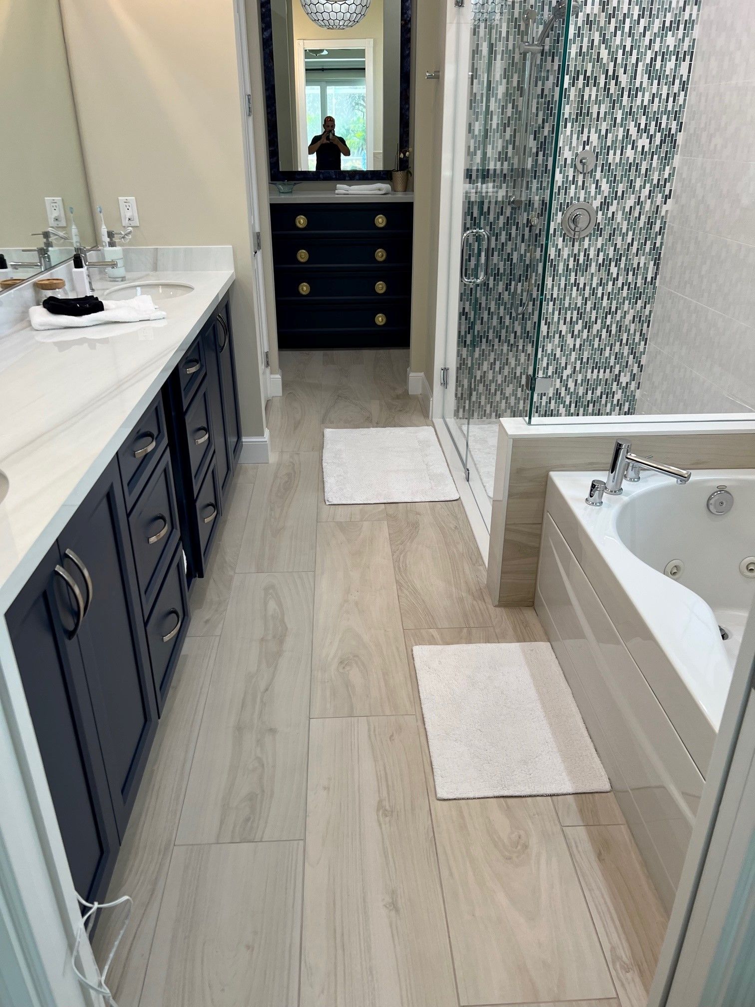 Bathroom with dark blue cabinets, white countertops, and a bathtub near a glass shower.
