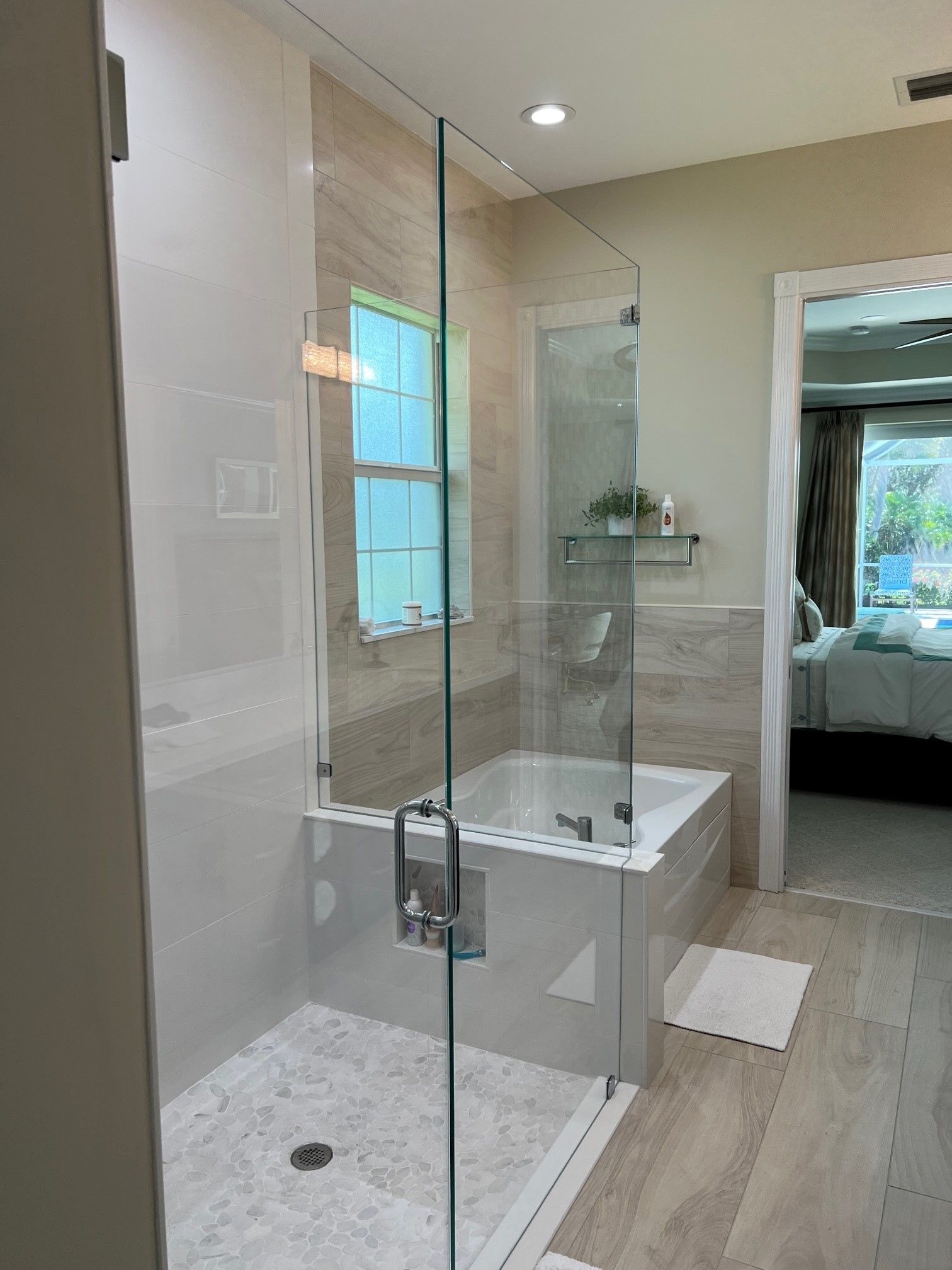 Modern bathroom with a glass shower and bathtub, neutral colors, and natural light.