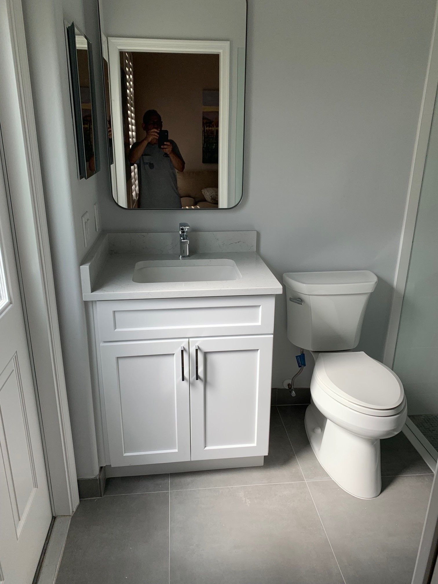 White bathroom vanity and toilet with a sink, mirror, and gray tiled floor.