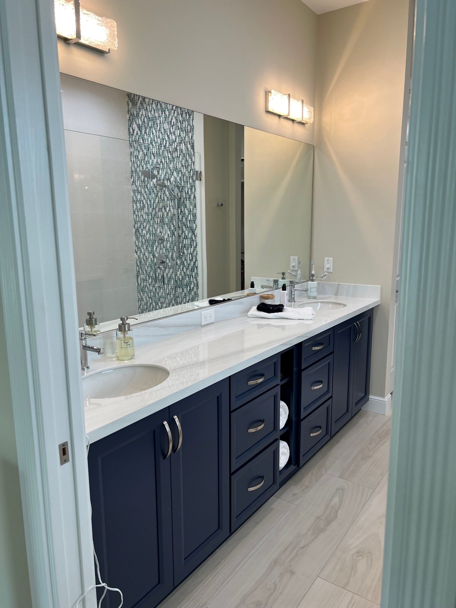 Dark blue double bathroom vanity with white countertop and sinks, mirrors, and wall tile.