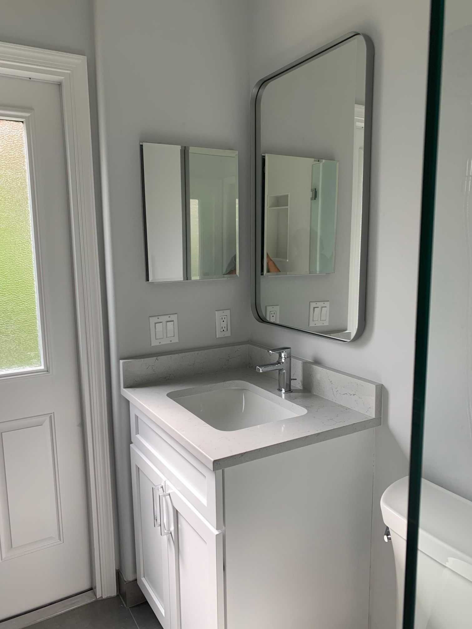 Bathroom with a white vanity, sink, and mirror with a grey countertop and white door.