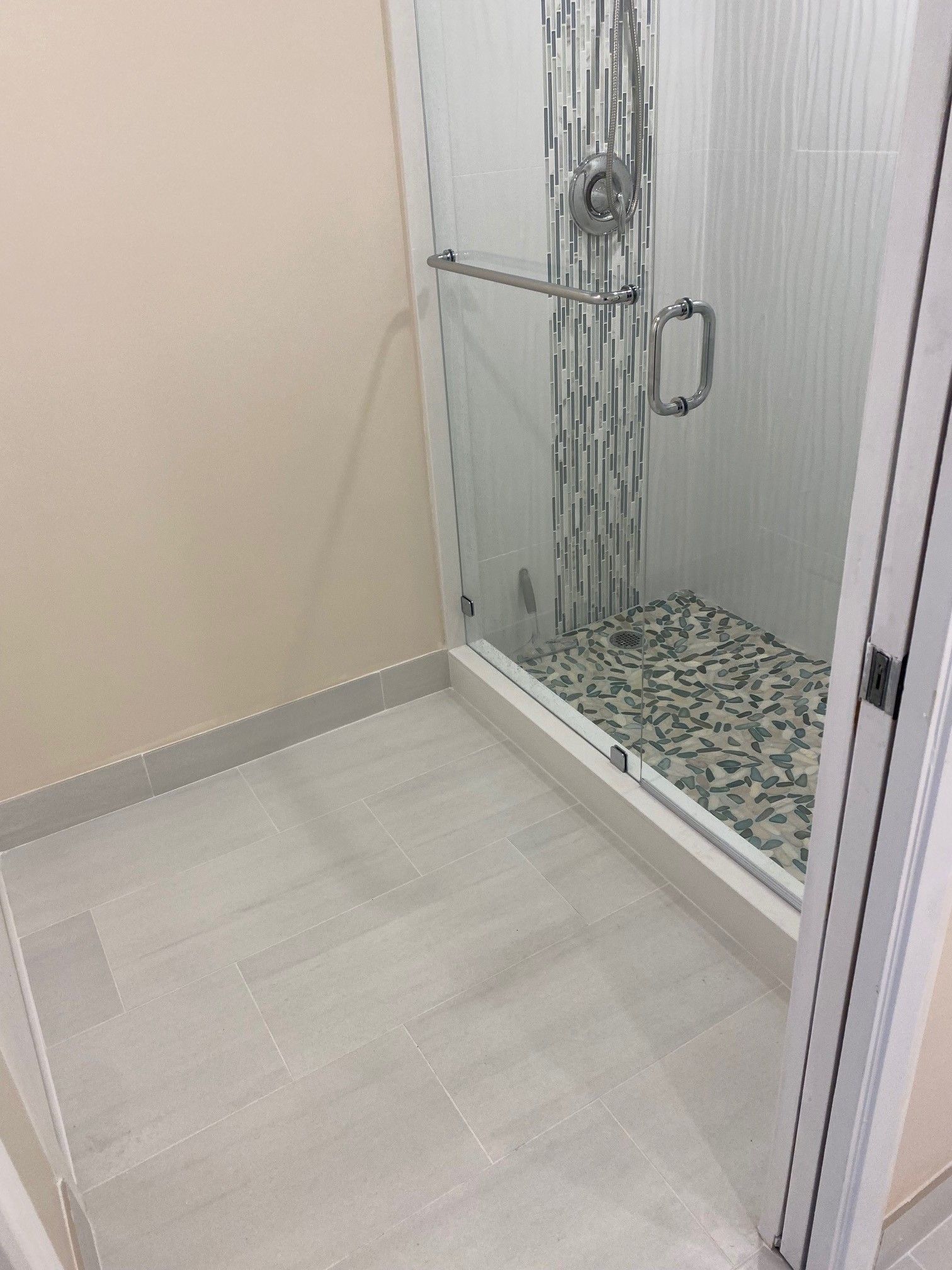 Shower stall with glass doors, tiled floor, and light beige walls.