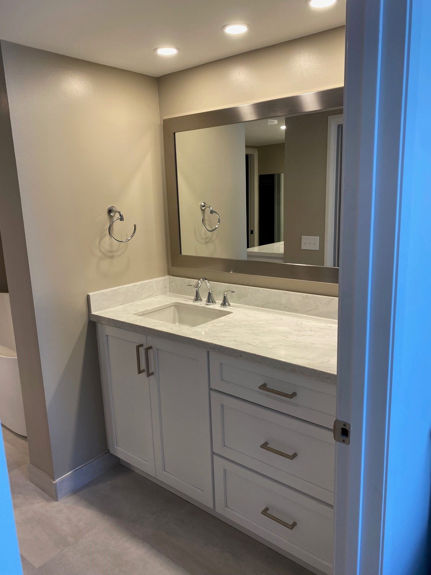 Bathroom with white cabinets, marble countertop, large mirror, and chrome fixtures.