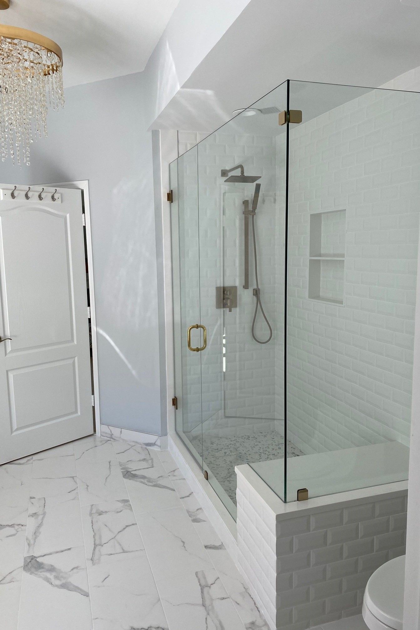 Modern bathroom with glass shower, white subway tile, and marble floor.
