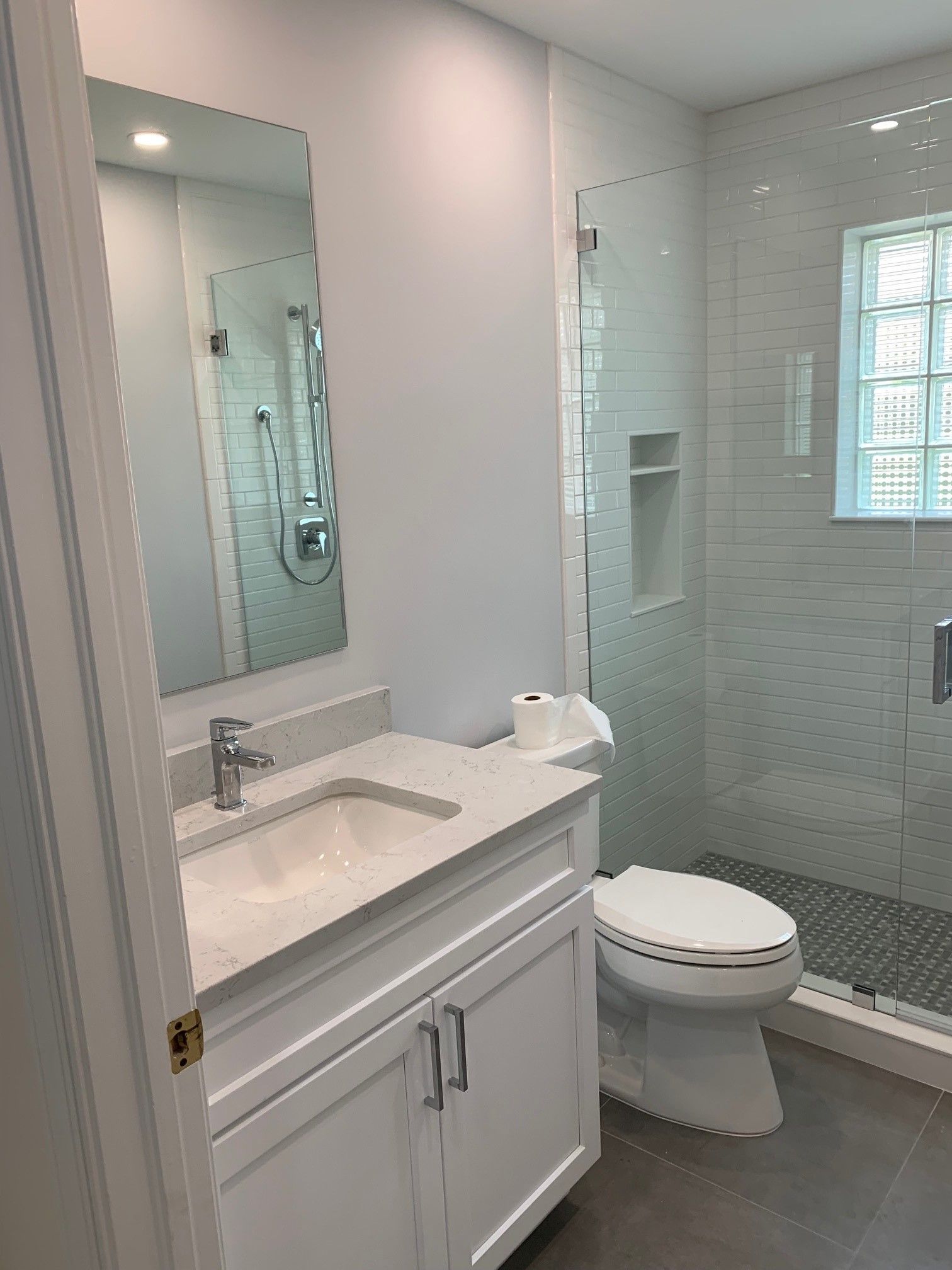White bathroom with vanity, toilet, and glass shower. Gray floor and white walls.
